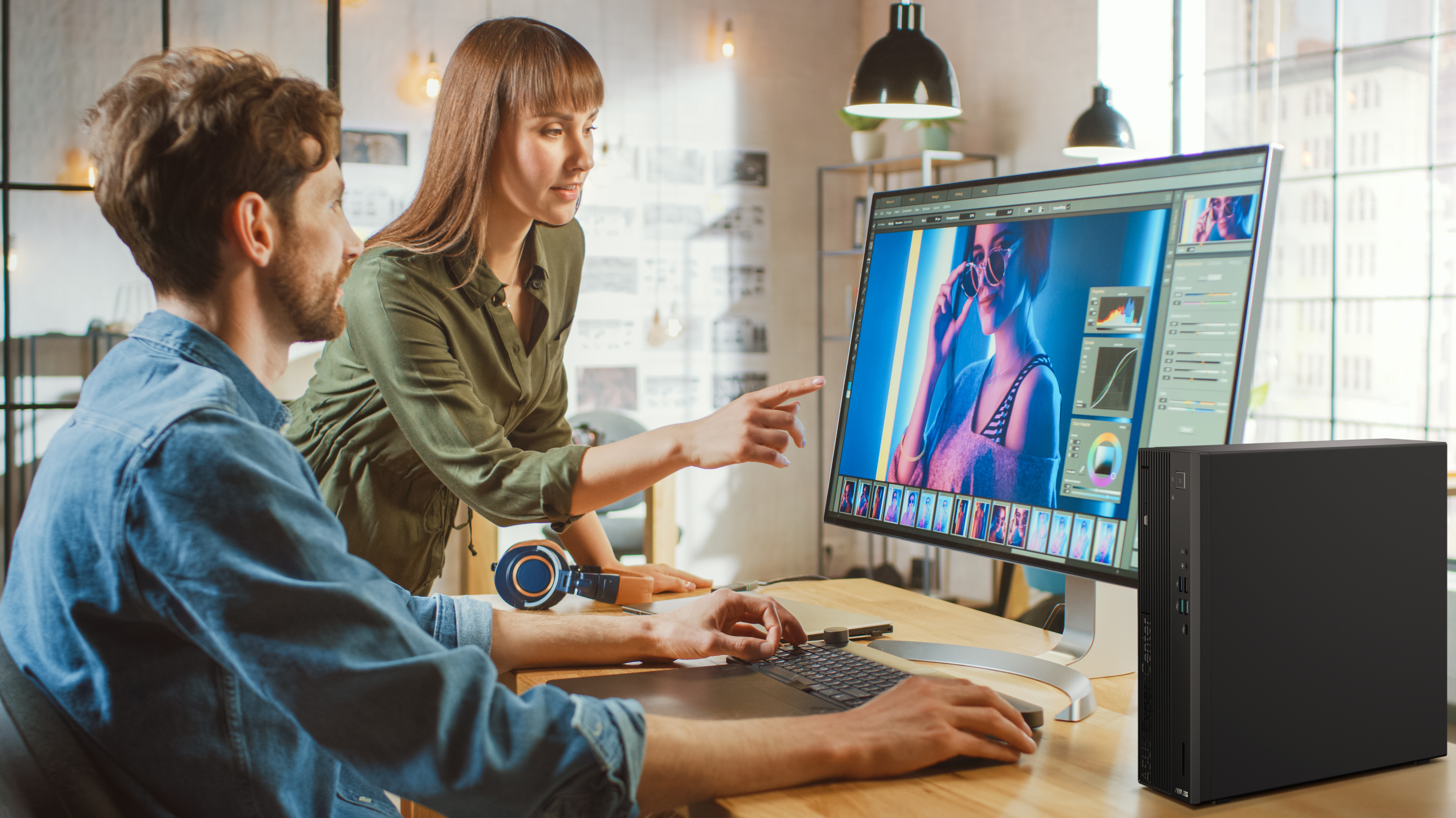 Two people working together on a computer, one points at the screen, a PC tower is visible.