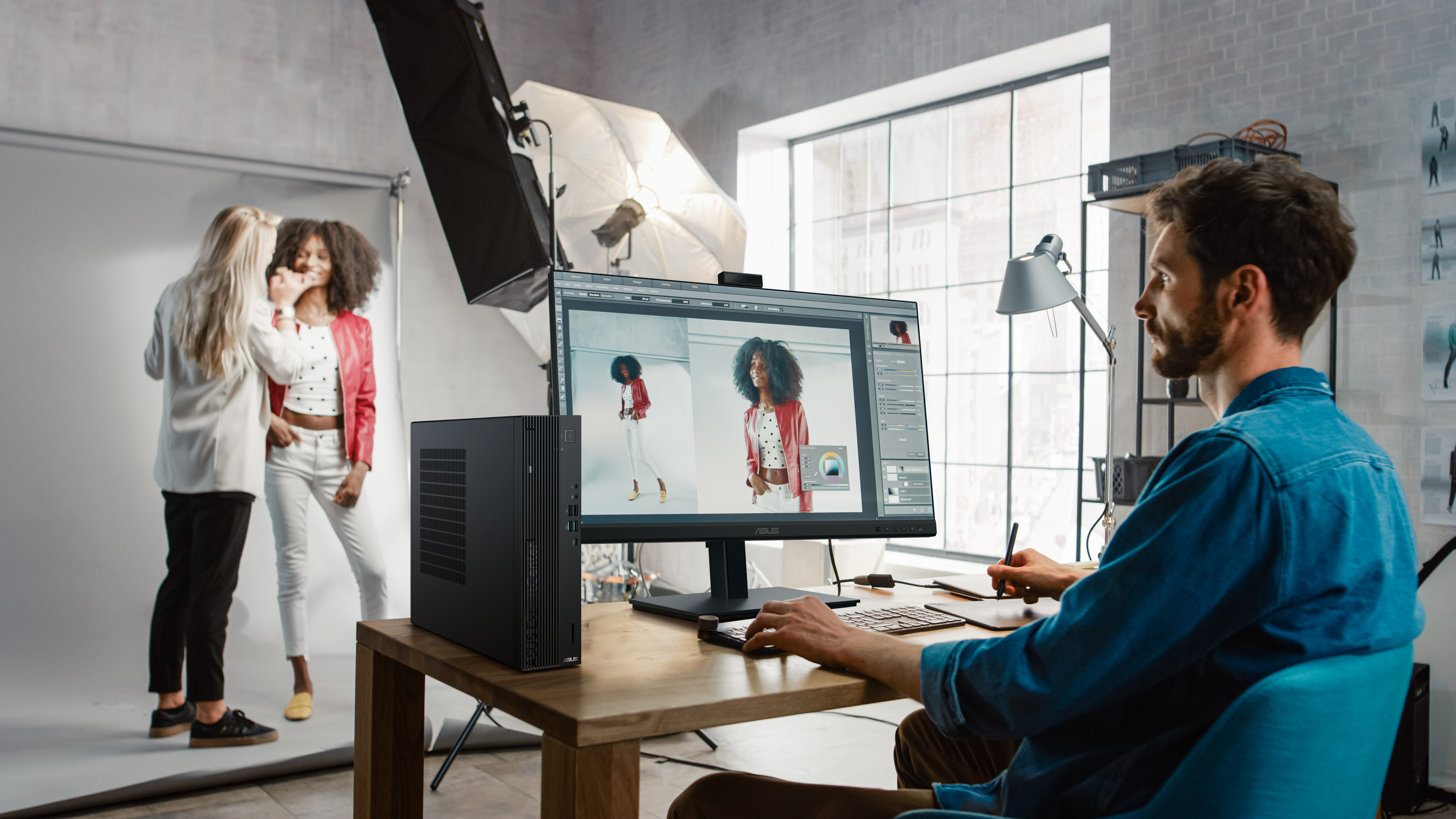Photographer working on computer, with models and lighting in background, studio setting.