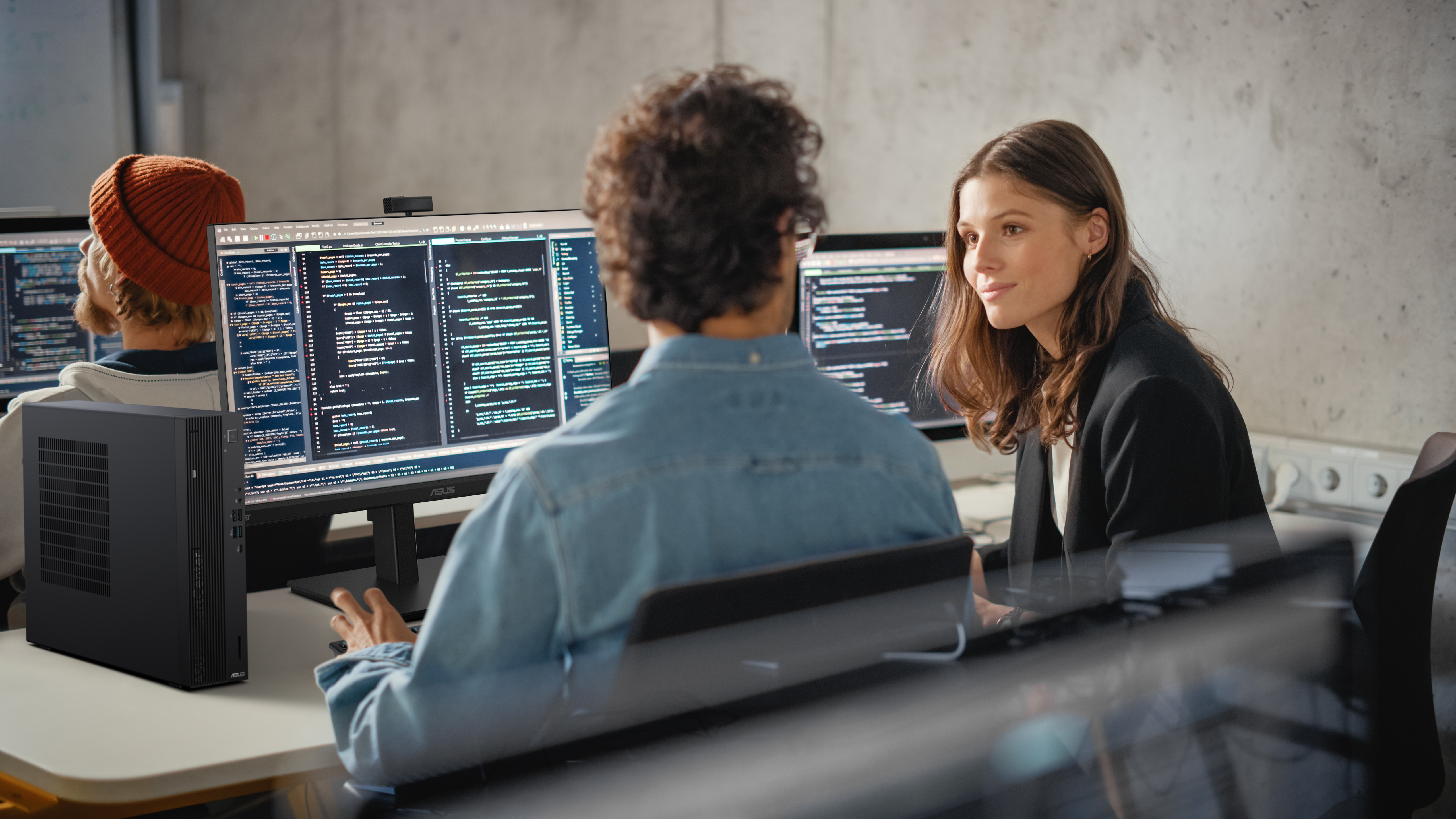 Two people working on computers with code. One woman and one man, in an office setting.