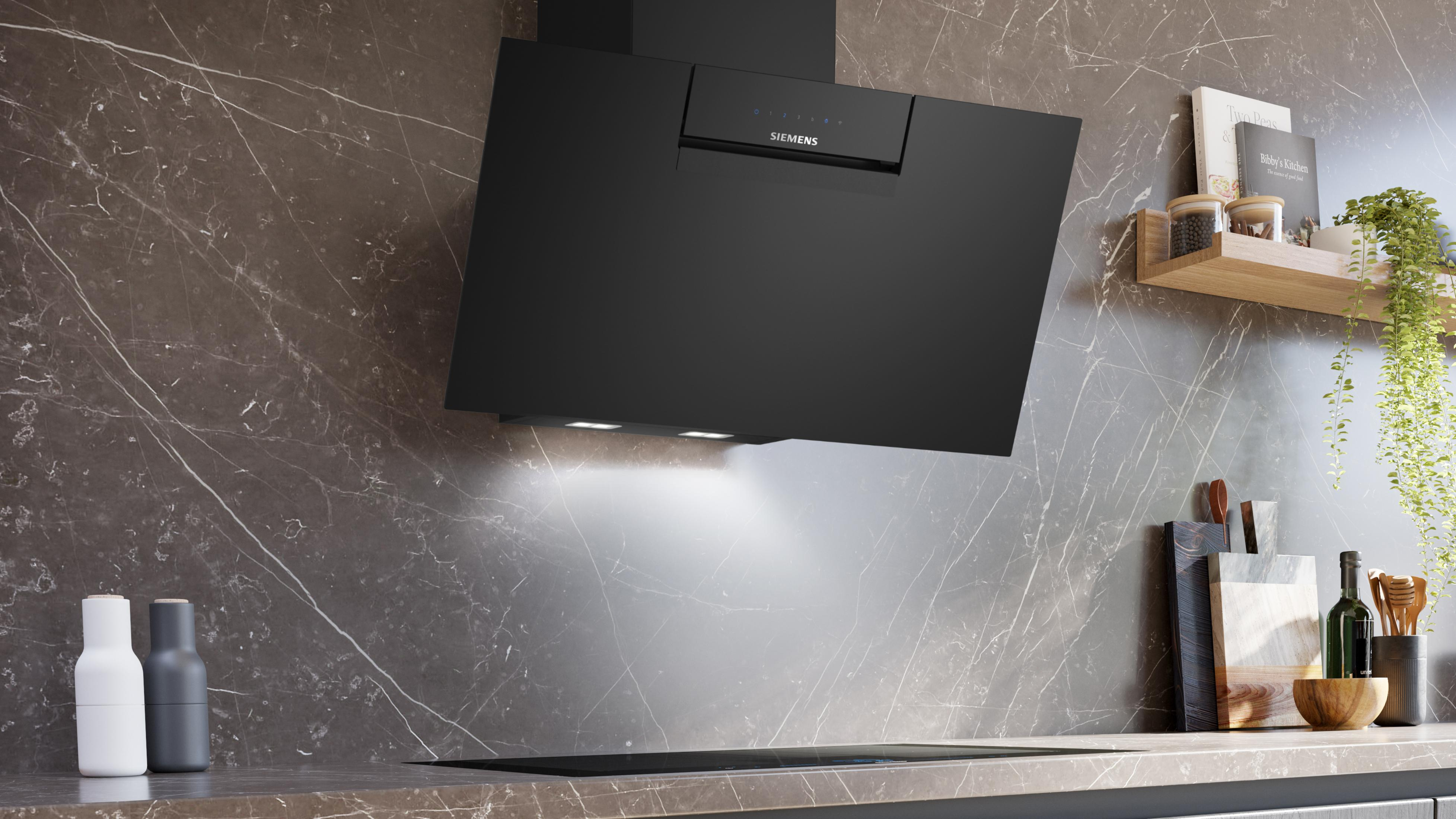 Black Siemens range hood above a cooktop, marble wall background.