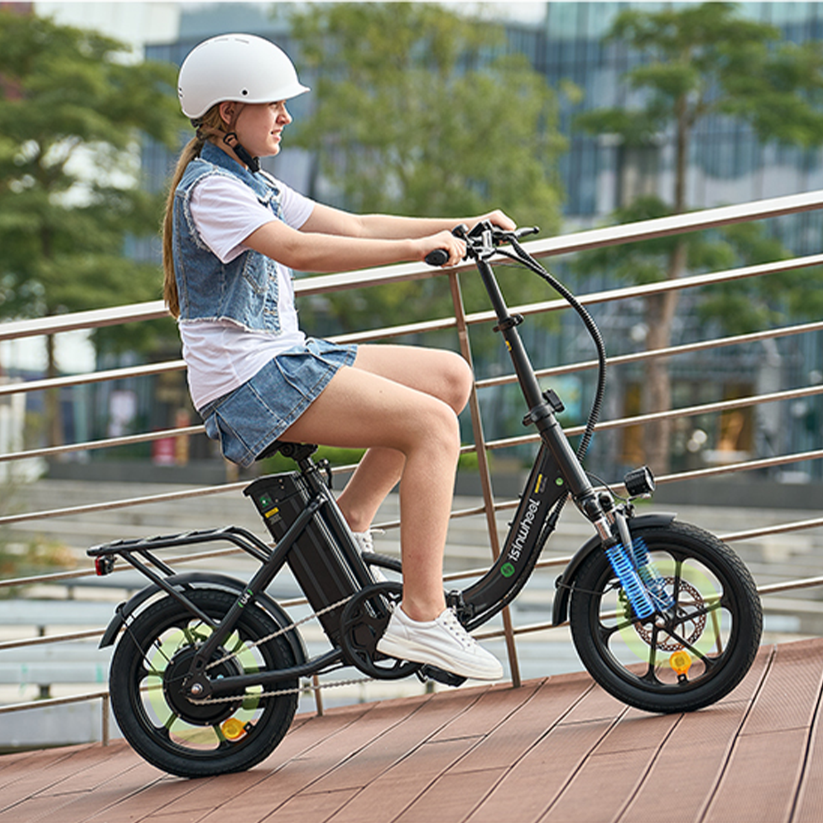 Dziewczyna jedzie na czarnym rowerze elektrycznym po drewnianej ścieżce. Ma kask i kurtkę dżinsową.