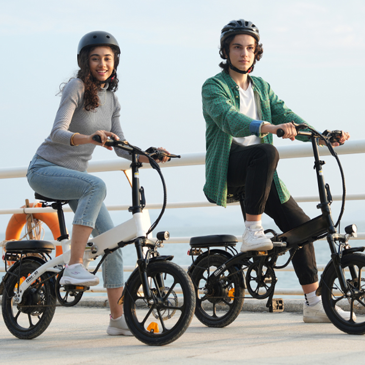 Dwie osoby na białych i czarnych rowerach elektrycznych, w kaskach, siedzące na molo.