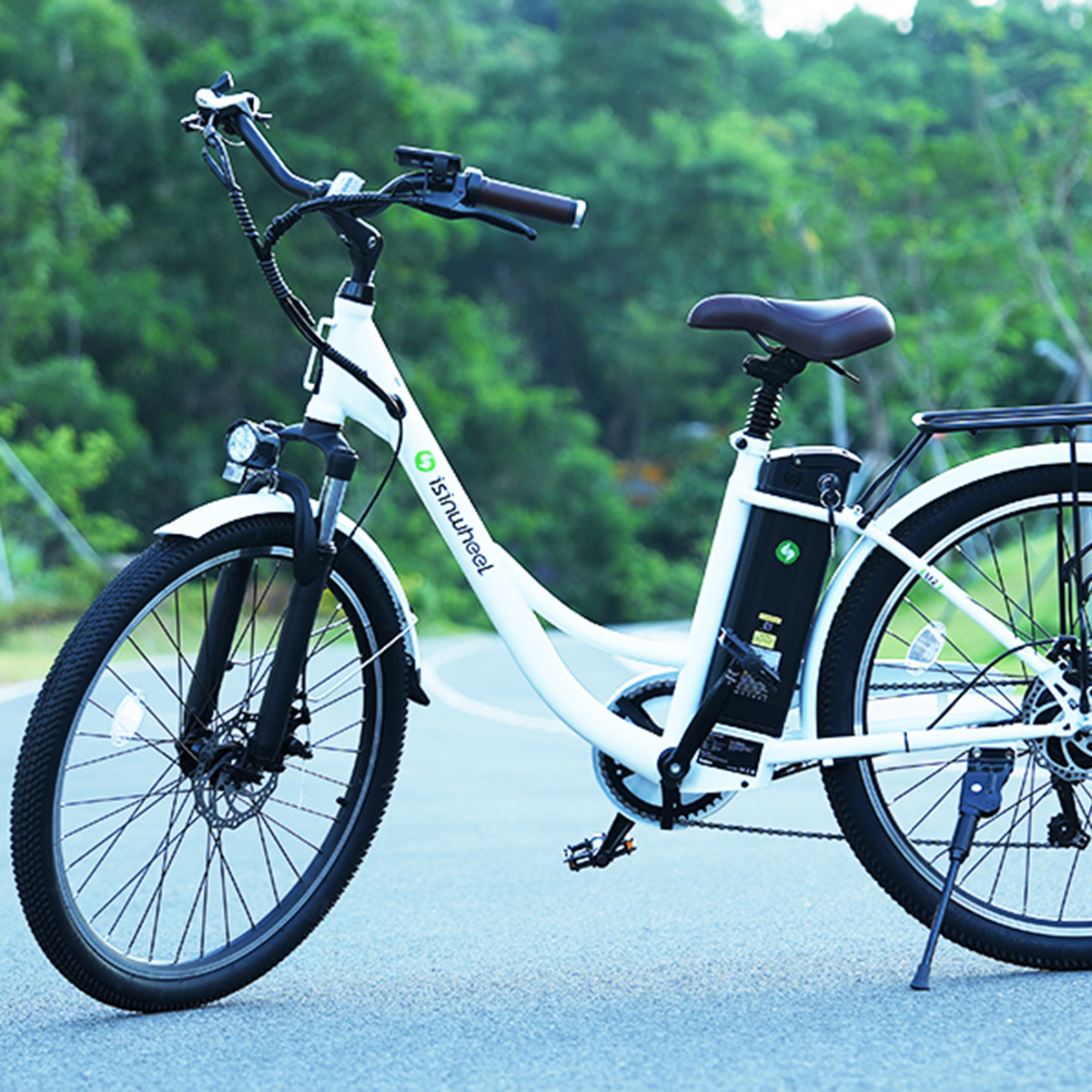 Biały rower elektryczny na drodze z zielonymi liśćmi w tle.