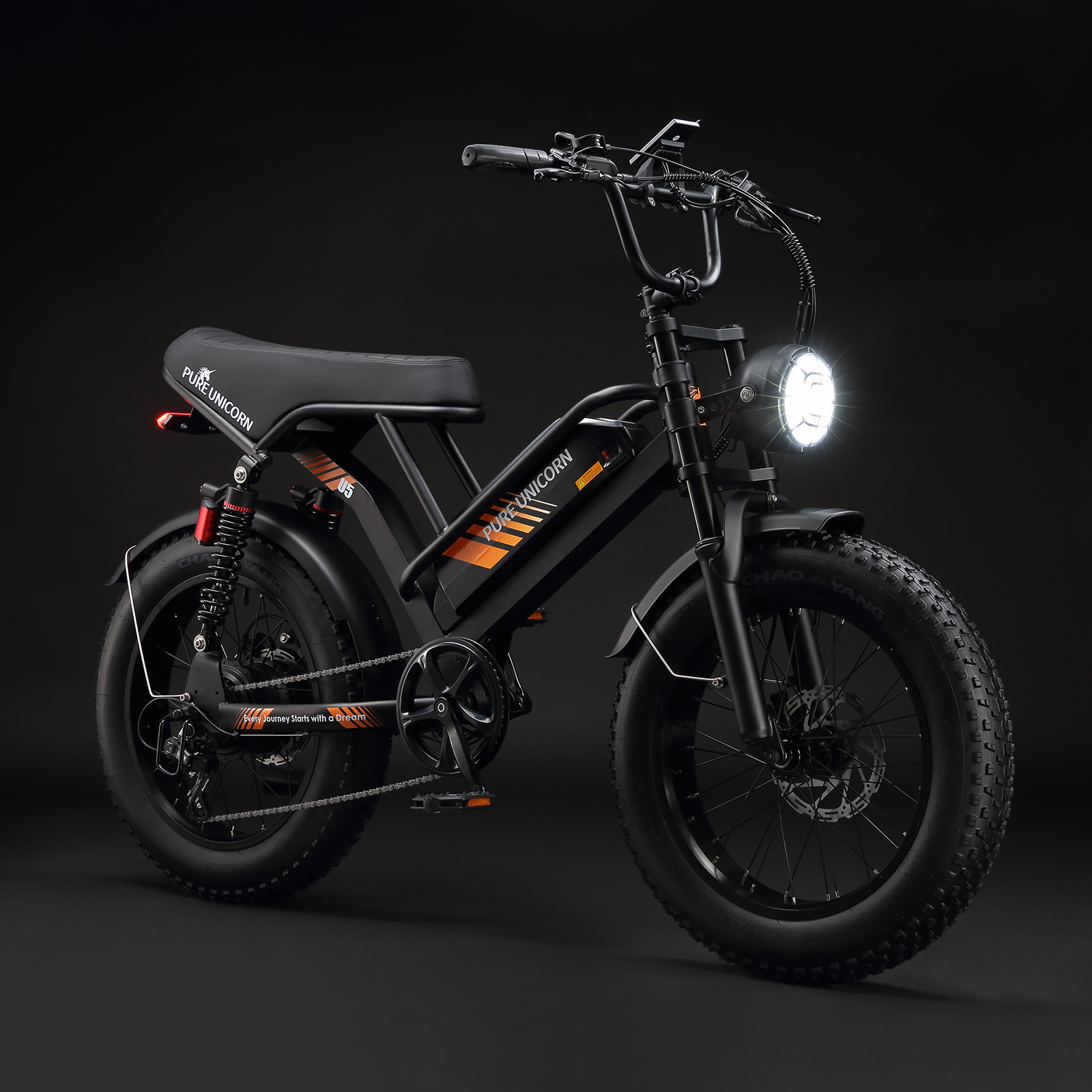 Czarny rower elektryczny z pomarańczowymi akcentami, dużymi oponami i jasnym reflektorem, na ciemnym tle.