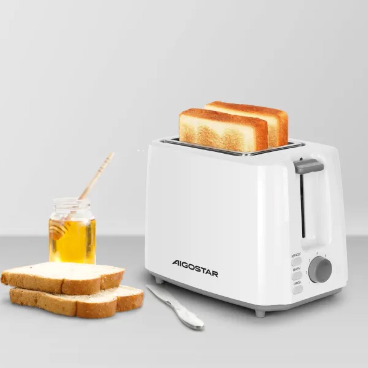 Biały toster z kromkami chleba. Miód i nóż po lewej stronie. Białe tło, toster i chleb.