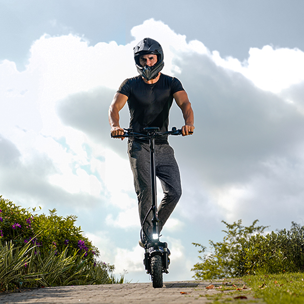 Mężczyzna w kasku jedzie czarną hulajnogą po utwardzonej drodze.