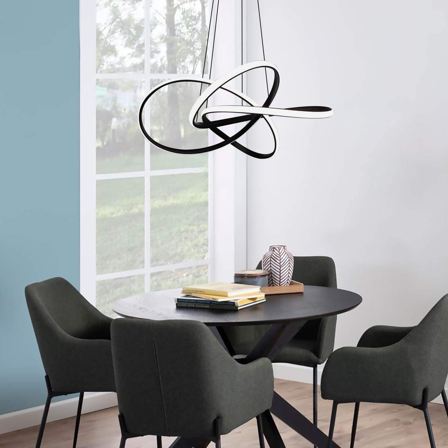 Moderne, verschlungene Leuchte über einem dunklen Tisch mit Stühlen. Hellblaue Wand, großes Fenster und Dekorationsartikel.