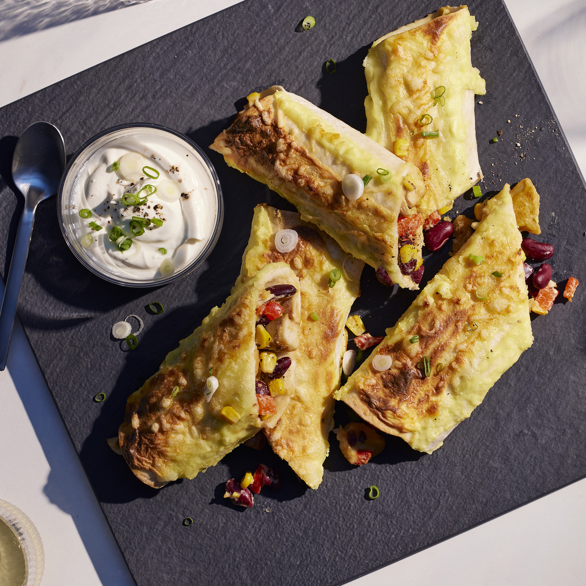 Draufsicht auf einen Schieferplatte mit gerolltem Essen, einer Schüssel Soße und einem Löffel.