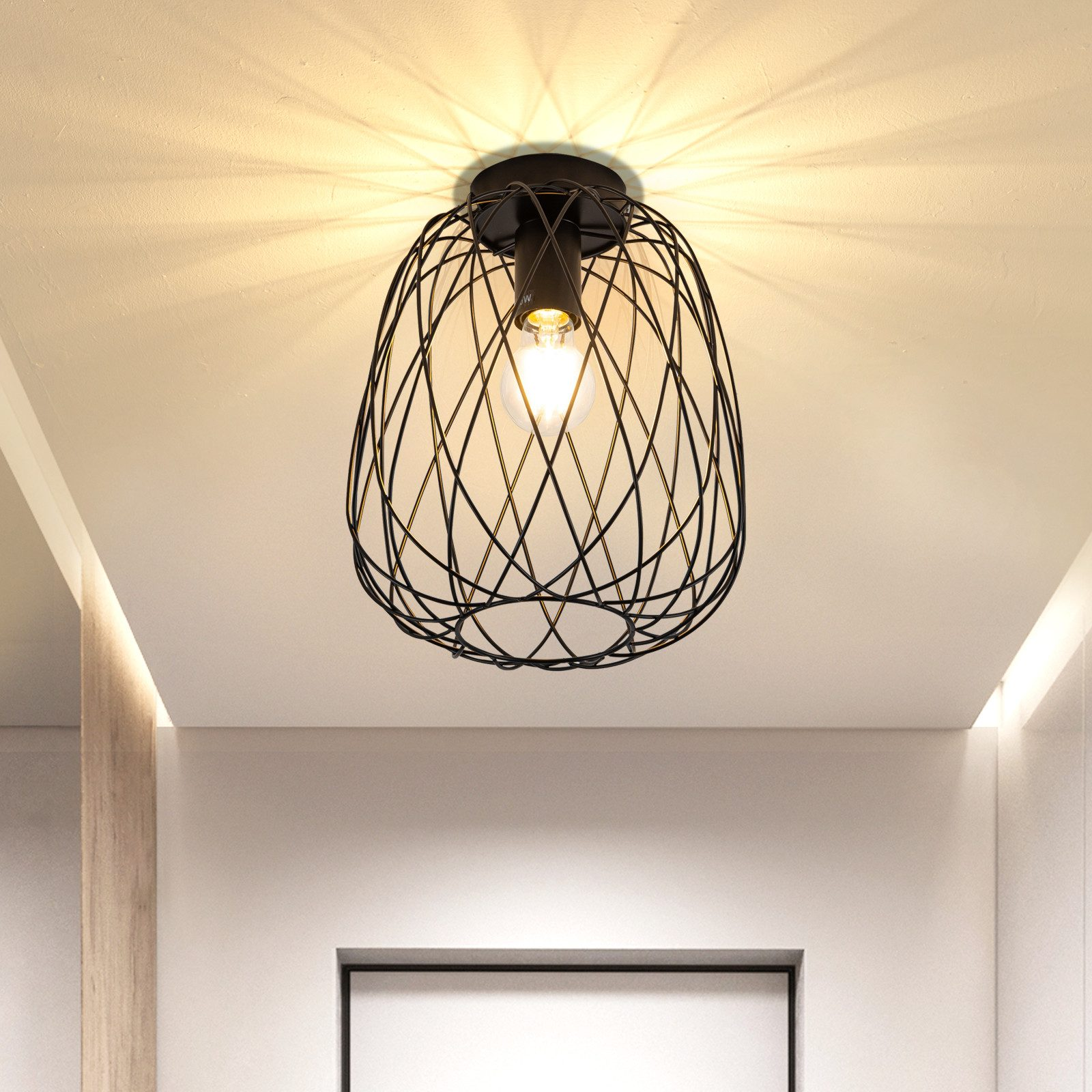 Lampada da soffitto. Forma ovale nera in filo metallico con lampadina all'interno, montata su soffitto bianco.