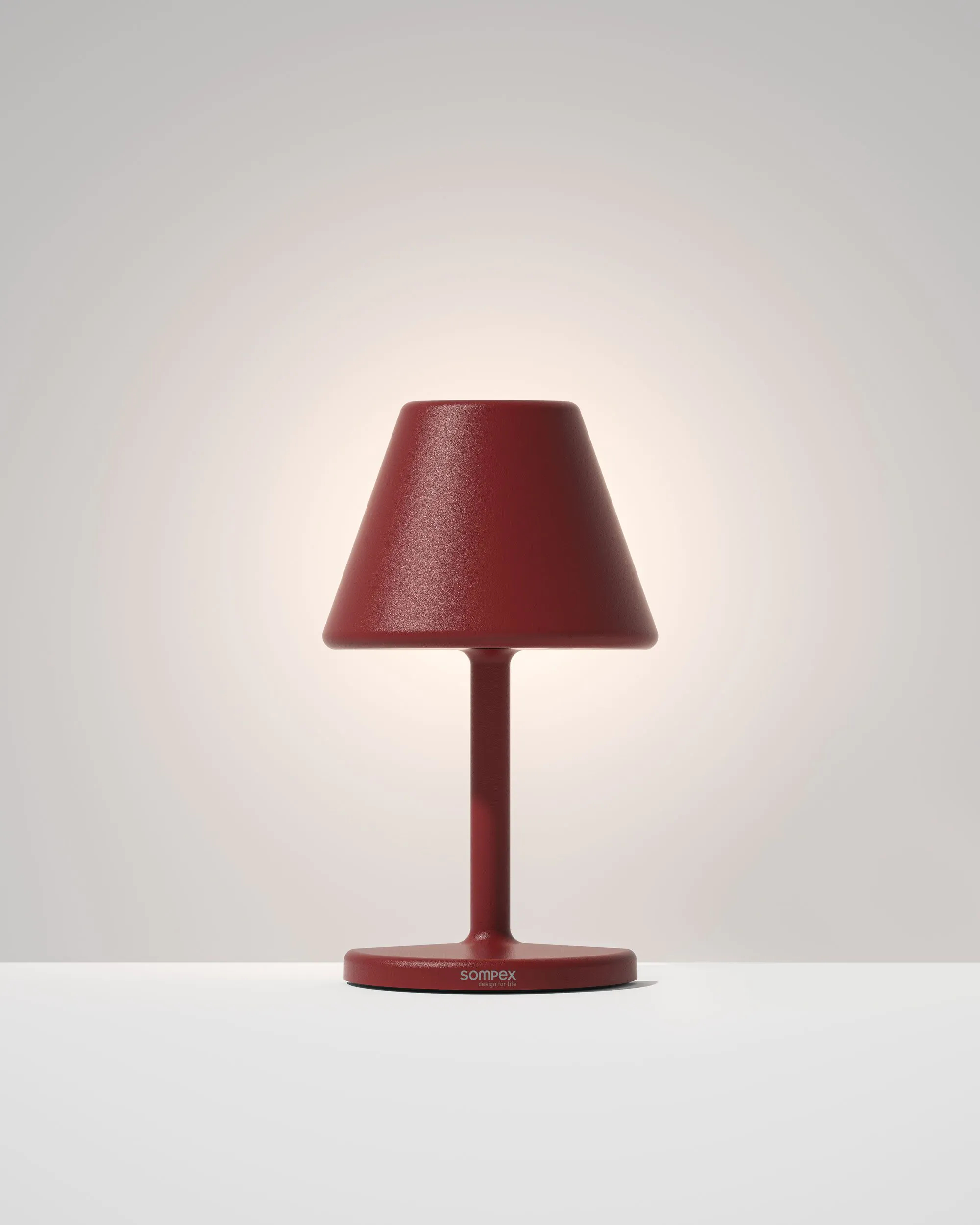 Una lampada da tavolo rossa con paralume e base. La lampada è su una superficie bianca.