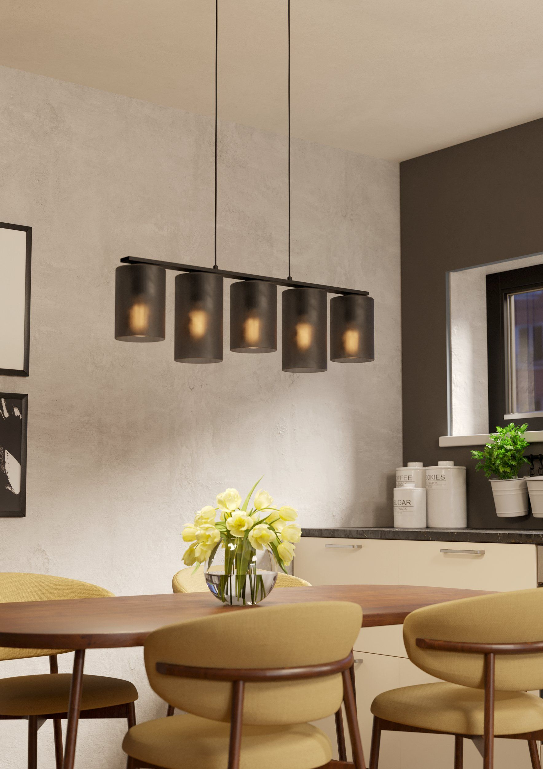 Un lampadario con cinque lampade cilindriche è appeso sopra un tavolo da pranzo con fiori e sedie in cucina.