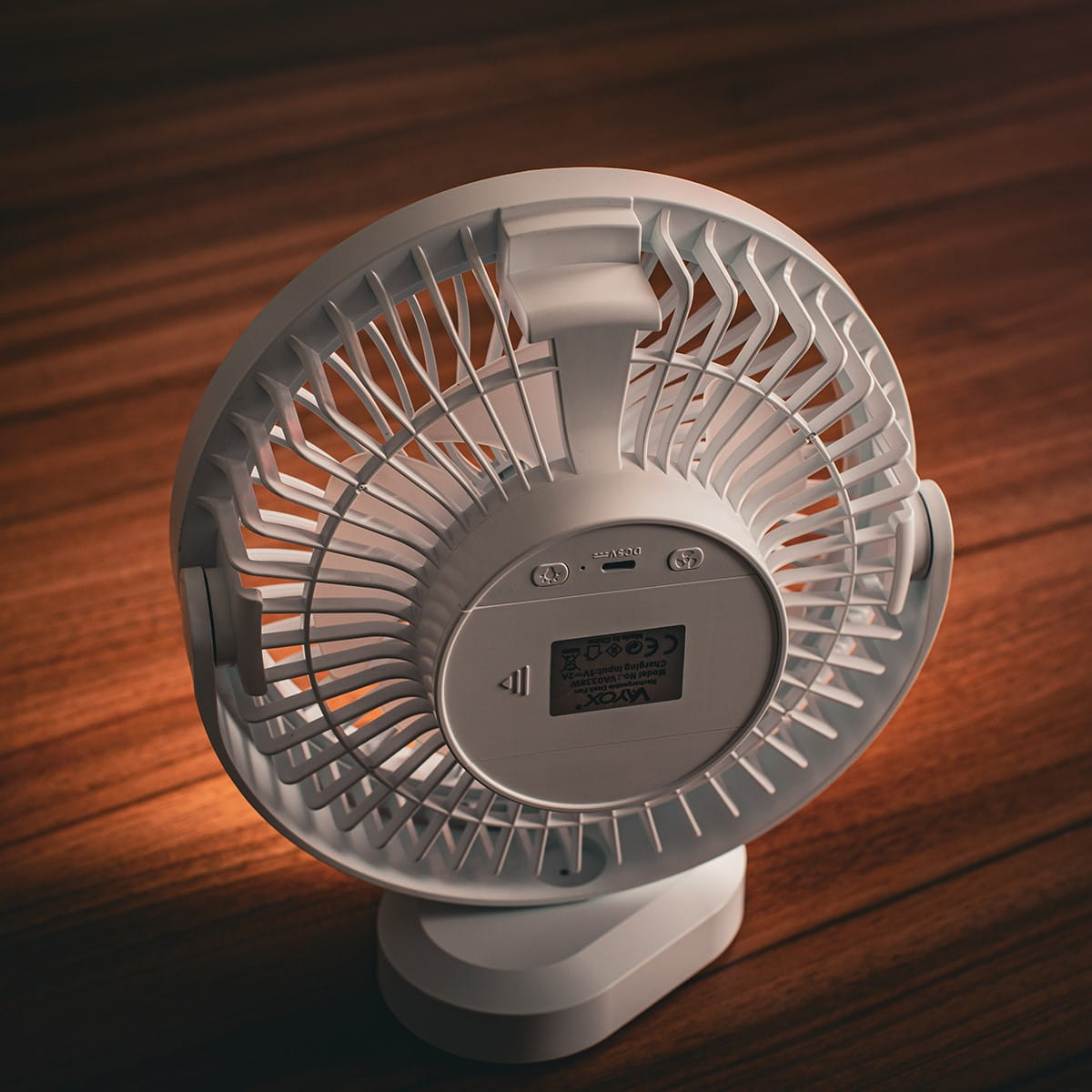 Tył białego wentylatora na ciemnej drewnianej powierzchni. Widoczne logo VAYOX.