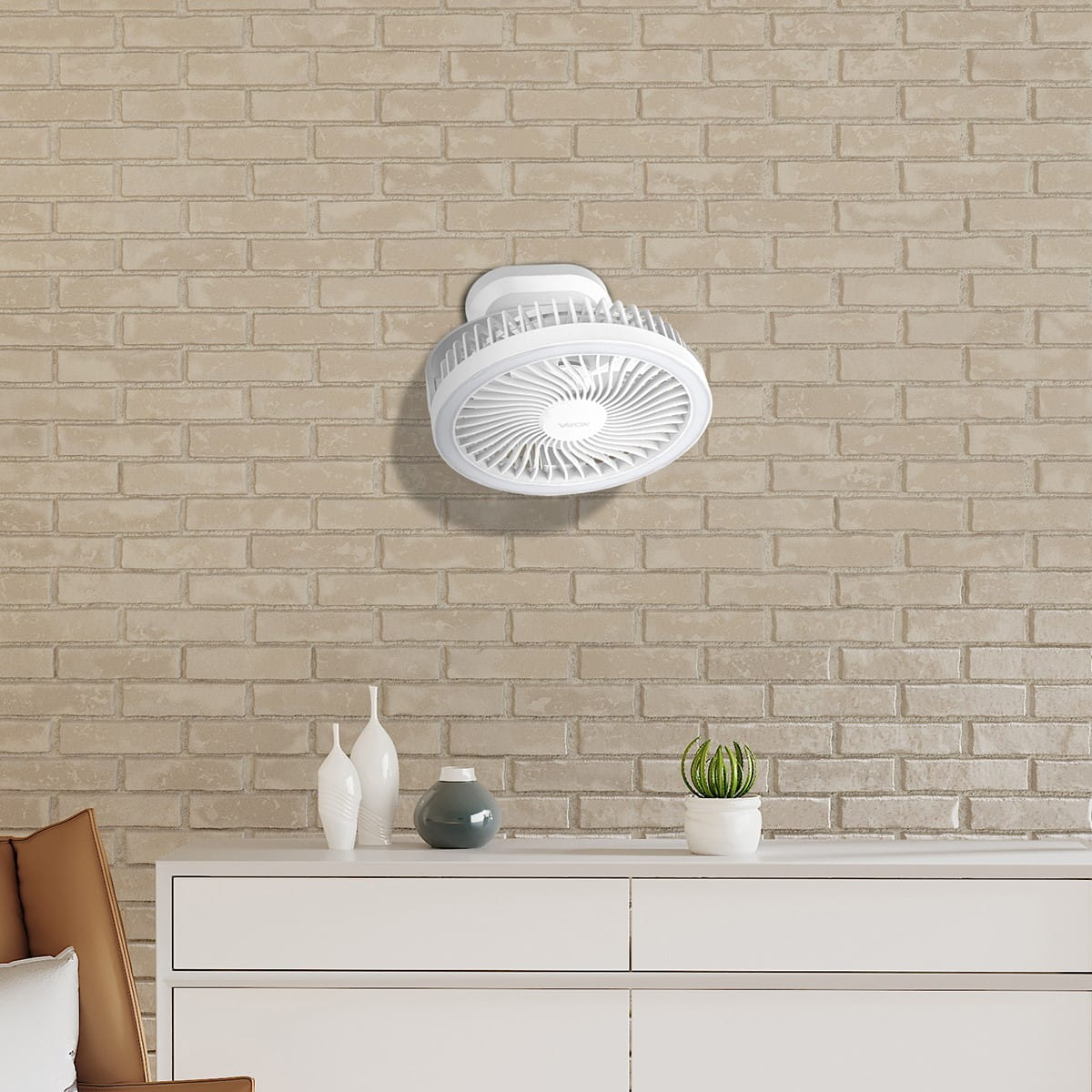 Biały wentylator zamontowany na ceglanej ścianie nad białą szafką z dekoracjami.