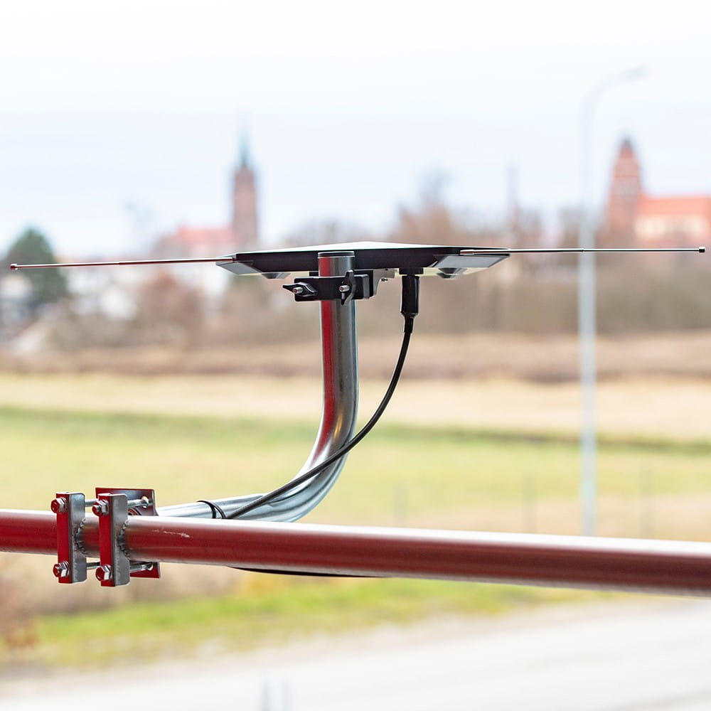 Antena zamontowana na czerwonej rurze, z miastem w tle. Antena ma dwa pręty.