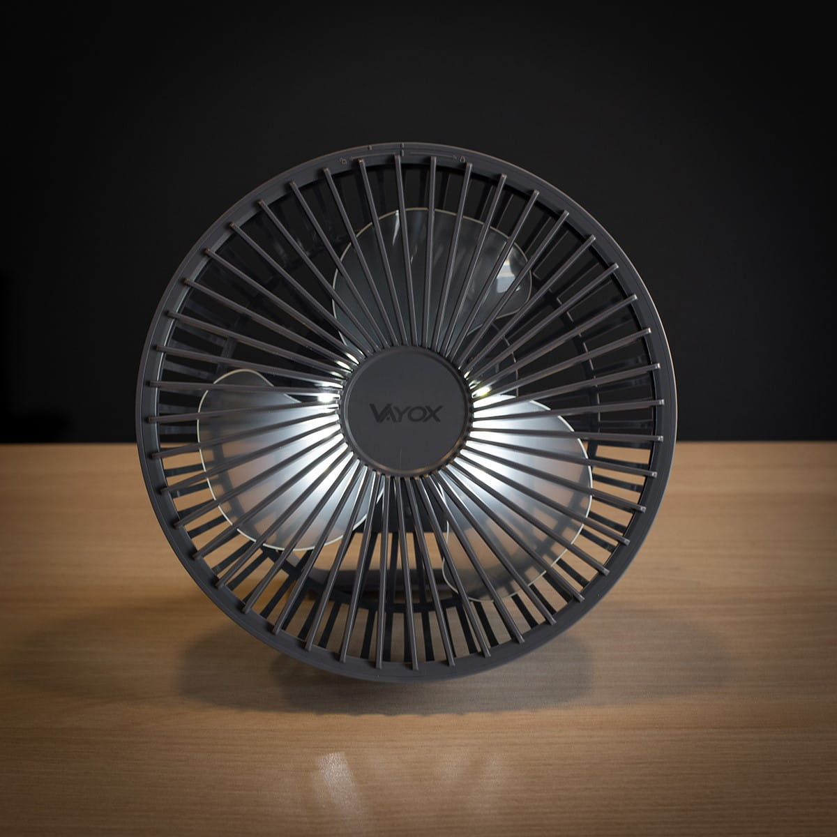 Czarny wentylator z trzema łopatkami. Wentylator stoi na drewnianej powierzchni z czarnym tłem.