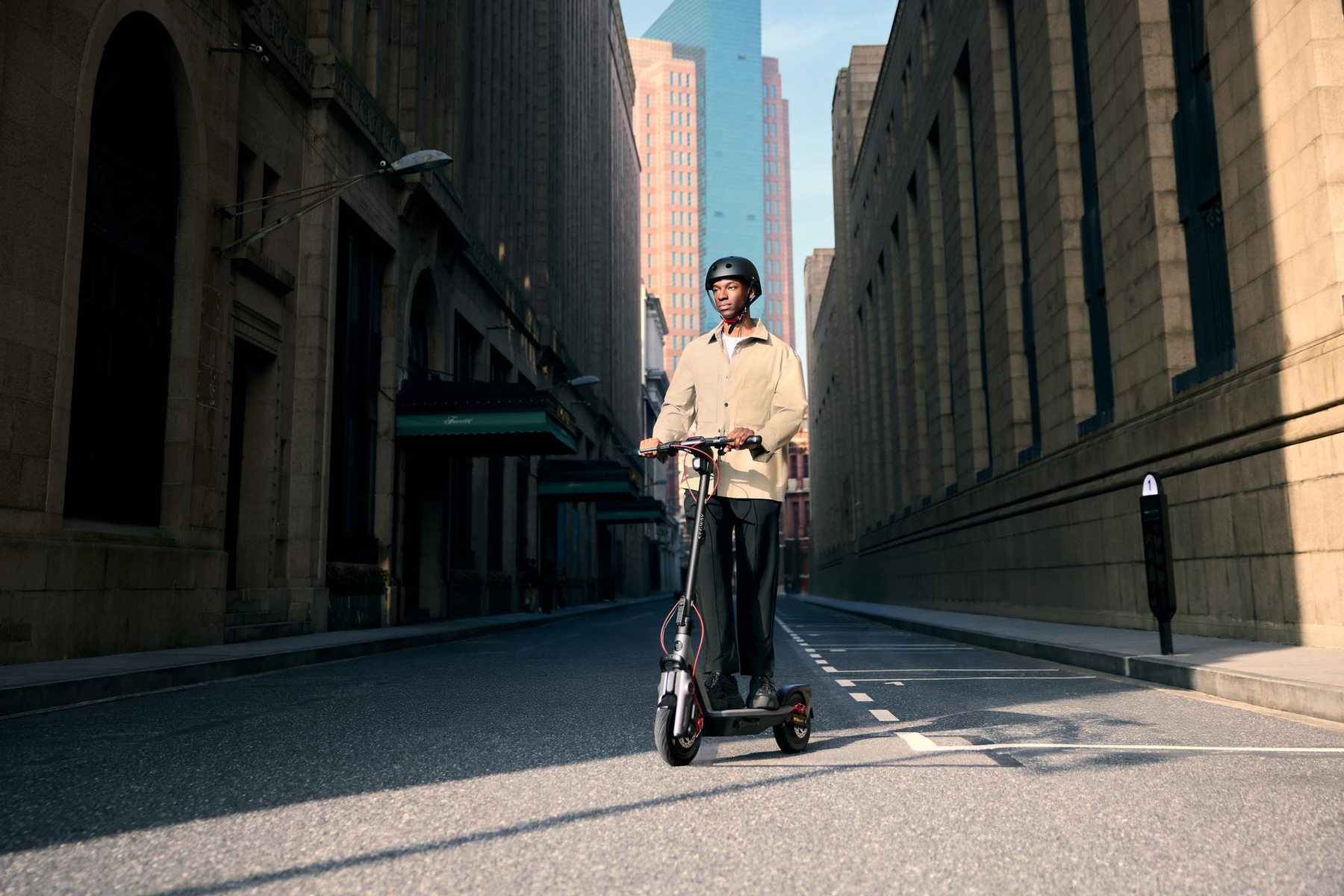 Hombre montando un patinete eléctrico por una calle de la ciudad, edificios a los lados.