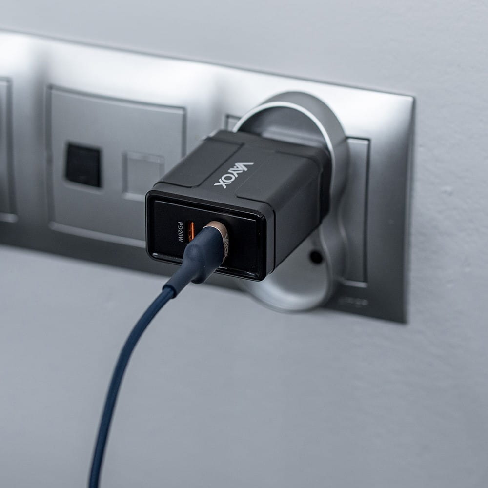 Czarna ładowarka Vayox podłączona do srebrnego gniazdka. Podłączony jest niebieski kabel.