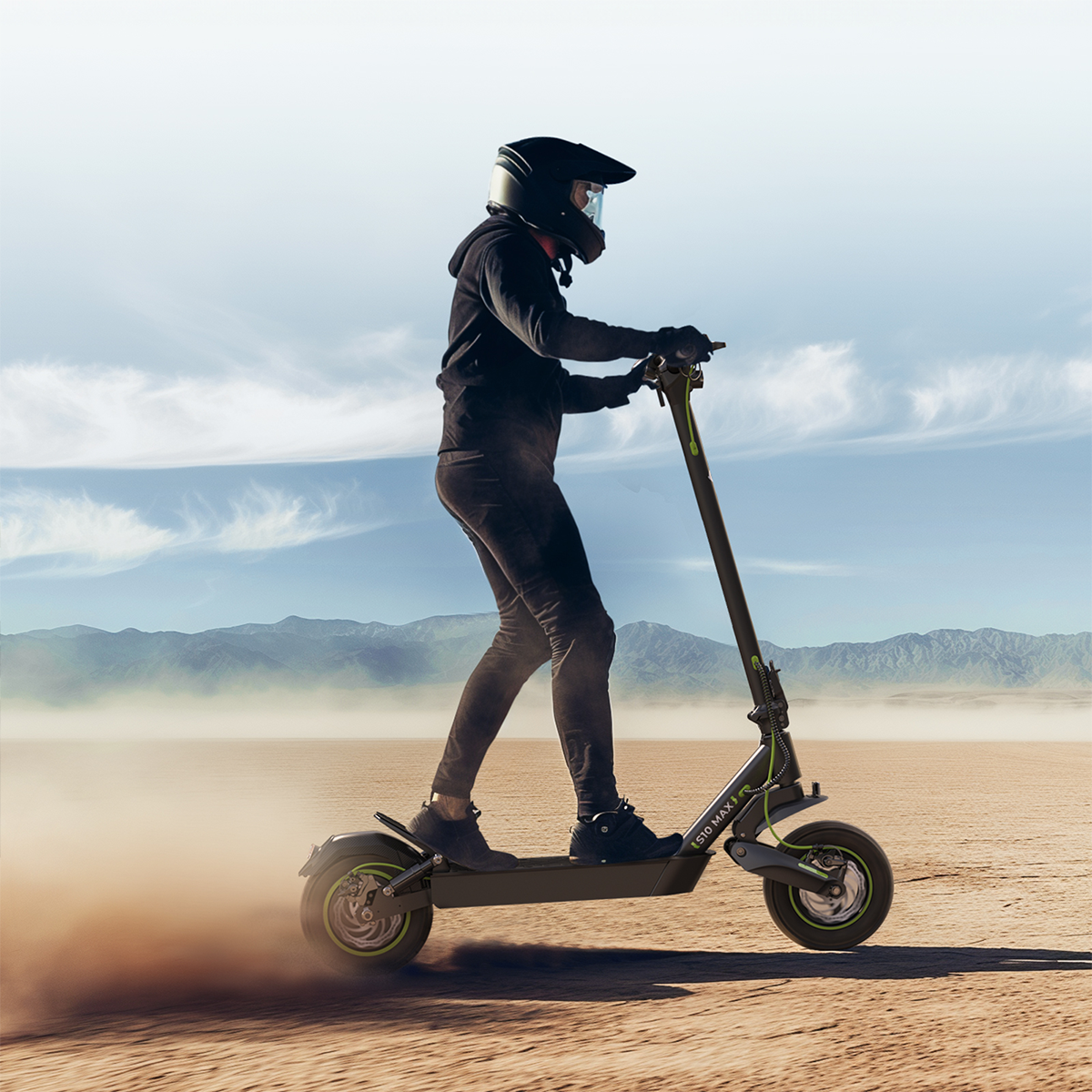 Osoba jedzie czarną hulajnogą elektryczną na pustynnej drodze. W tle góry.