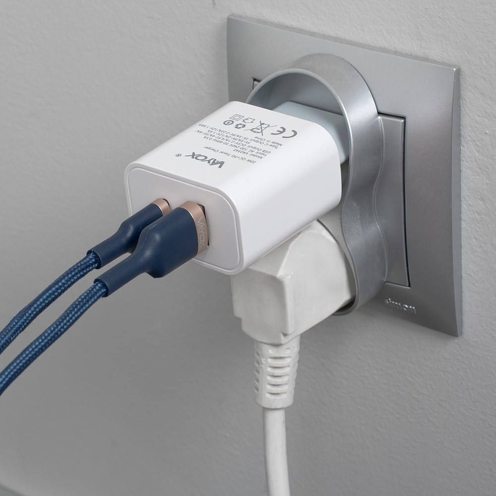 Biała ładowarka Vayox podłączona do gniazdka, z drugim wtykiem poniżej.