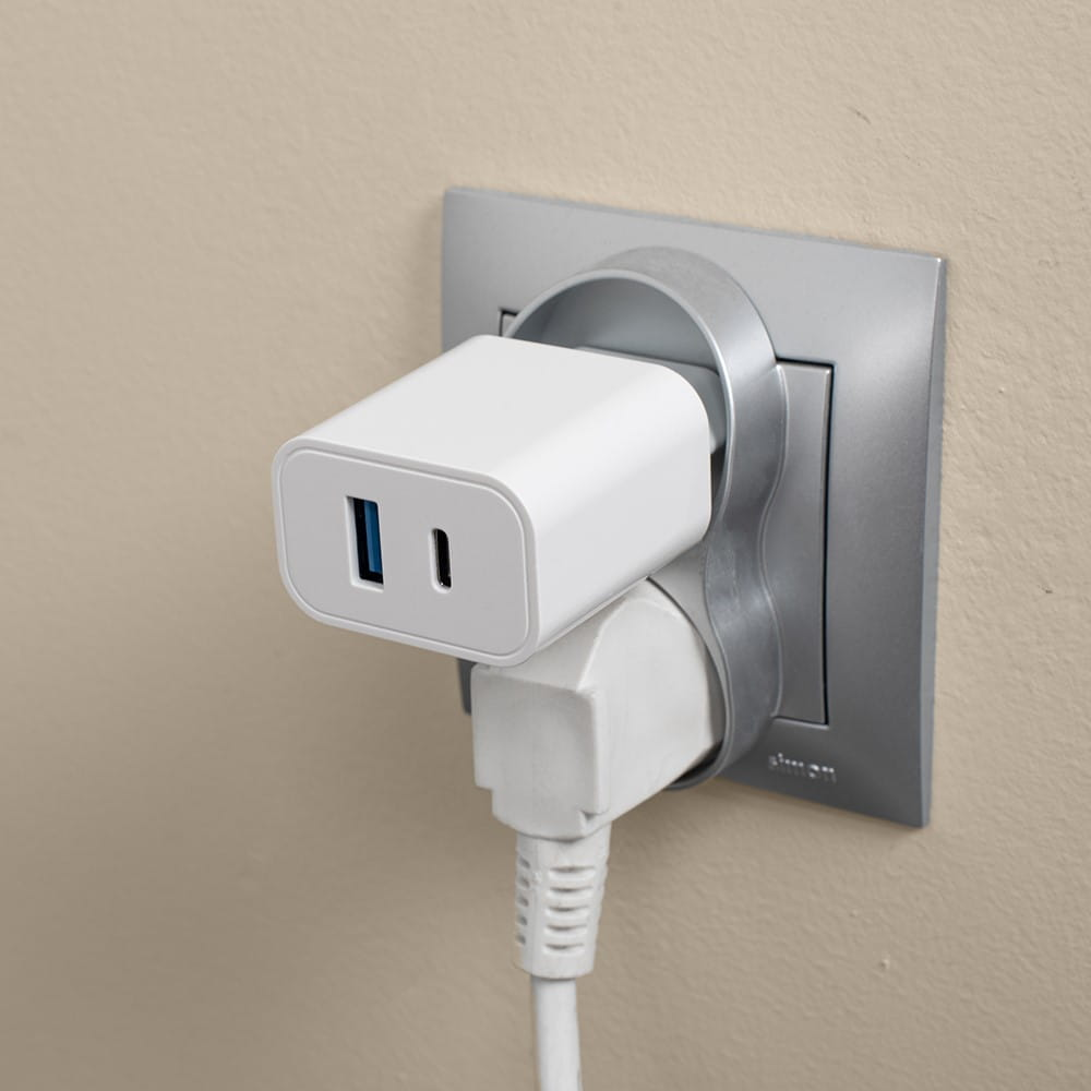 Biała ładowarka w gniazdku ściennym. Biała ściana i szara ramka gniazdka.