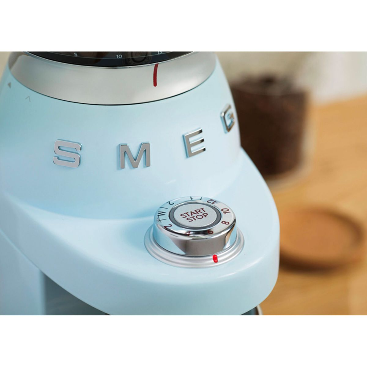 Gros plan sur un moulin à café Smeg bleu clair. Le cadran marche/arrêt et le logo SMEG sont visibles.