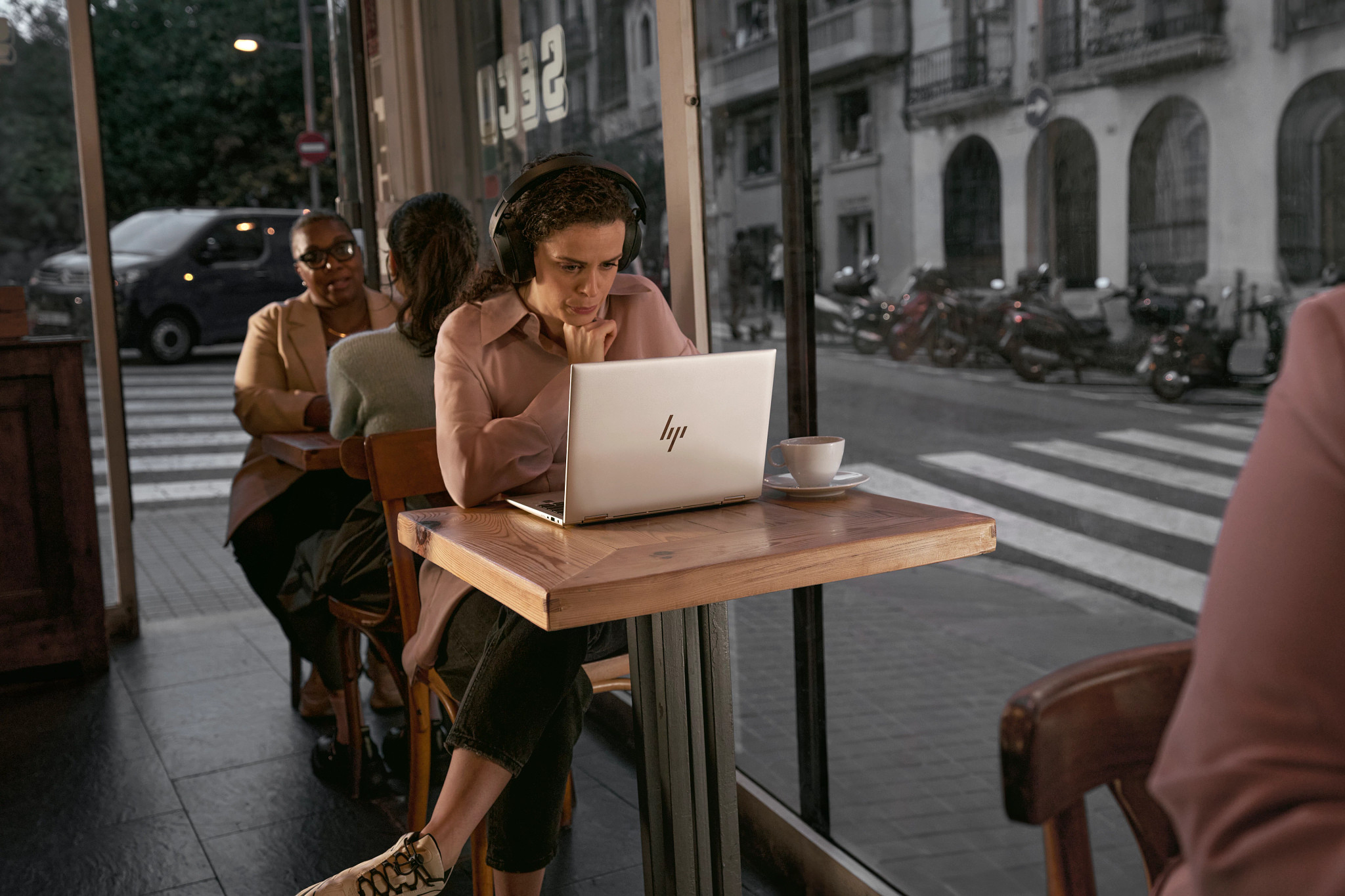 Donna in un bar che usa un laptop. Altre persone e tavoli sullo sfondo. Caffè sul tavolo.