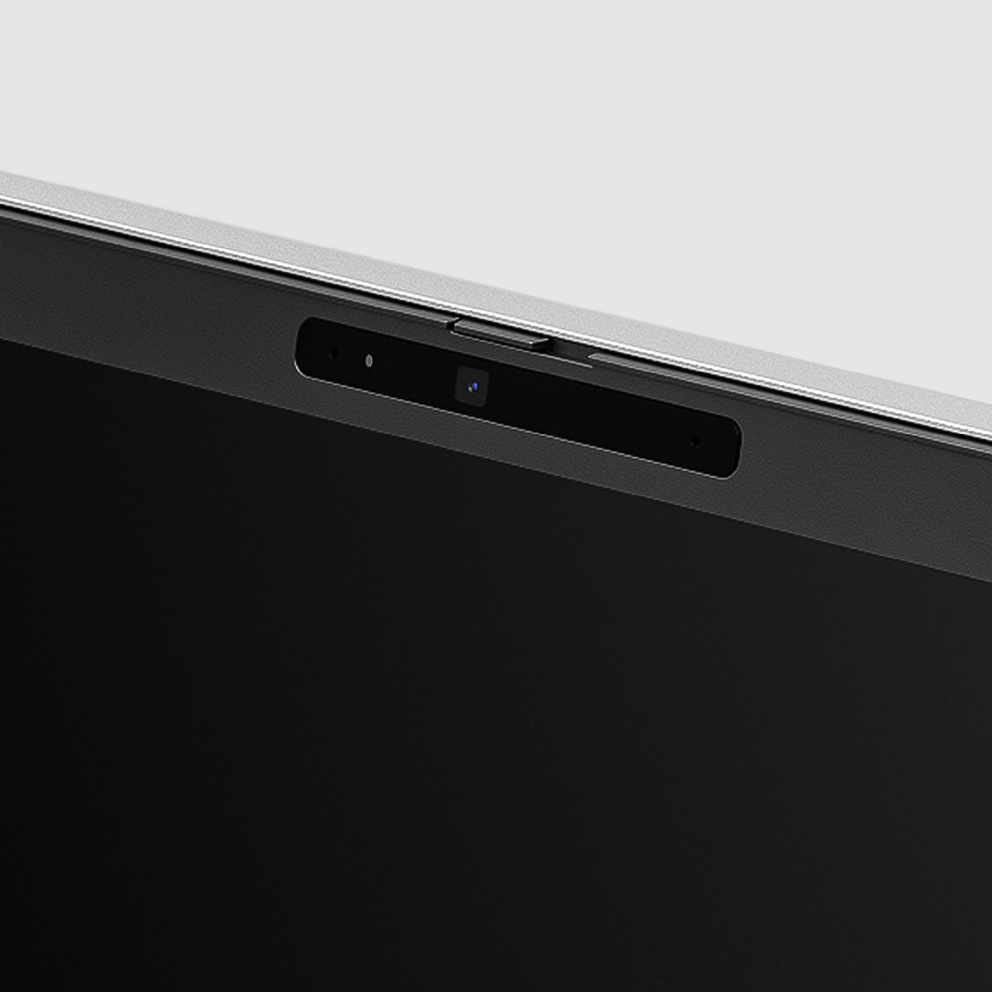 Primo piano della fotocamera e del microfono del laptop, cornice nera su sfondo grigio chiaro.