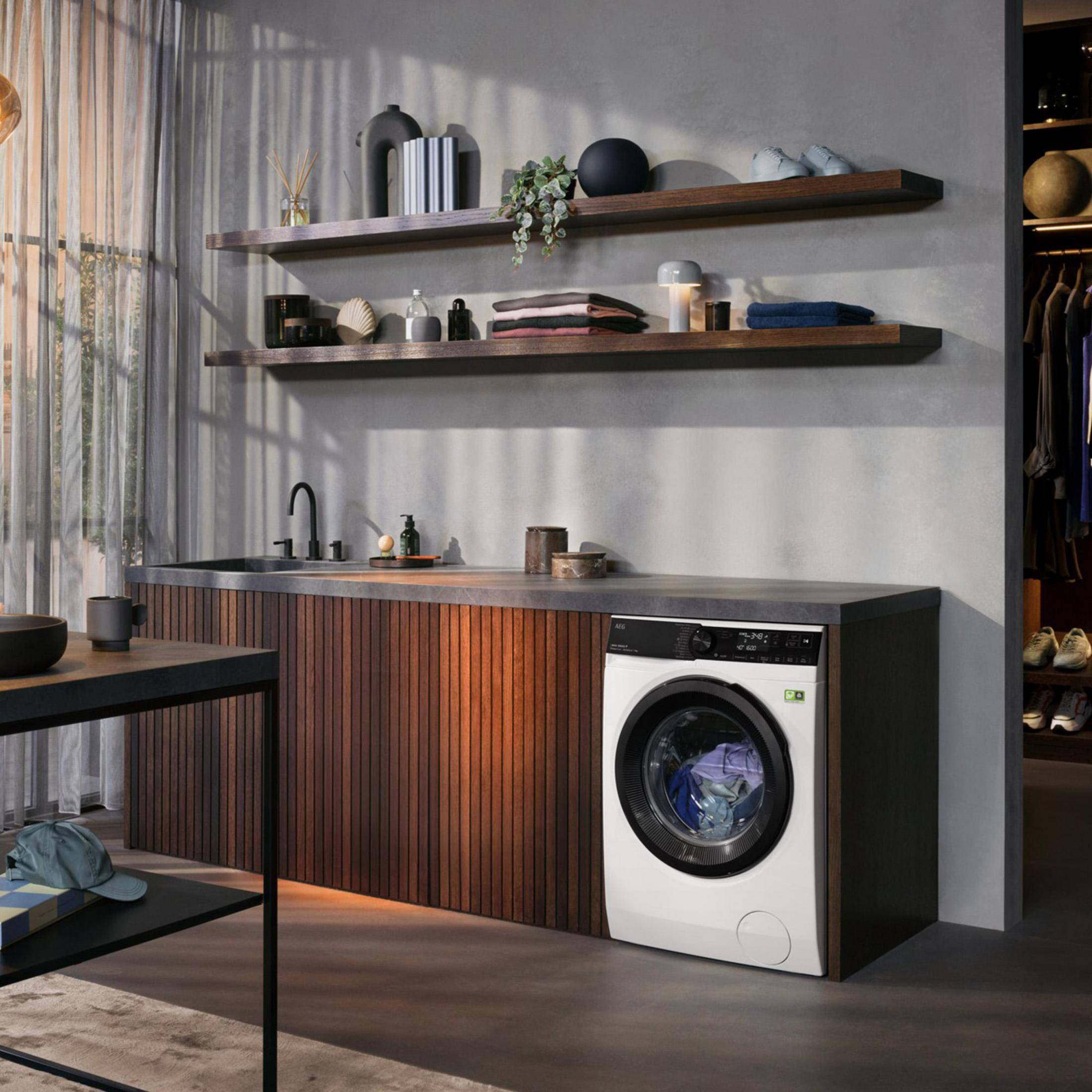 Biała pralka w pralni z półkami, blatem i drewnianymi ścianami.