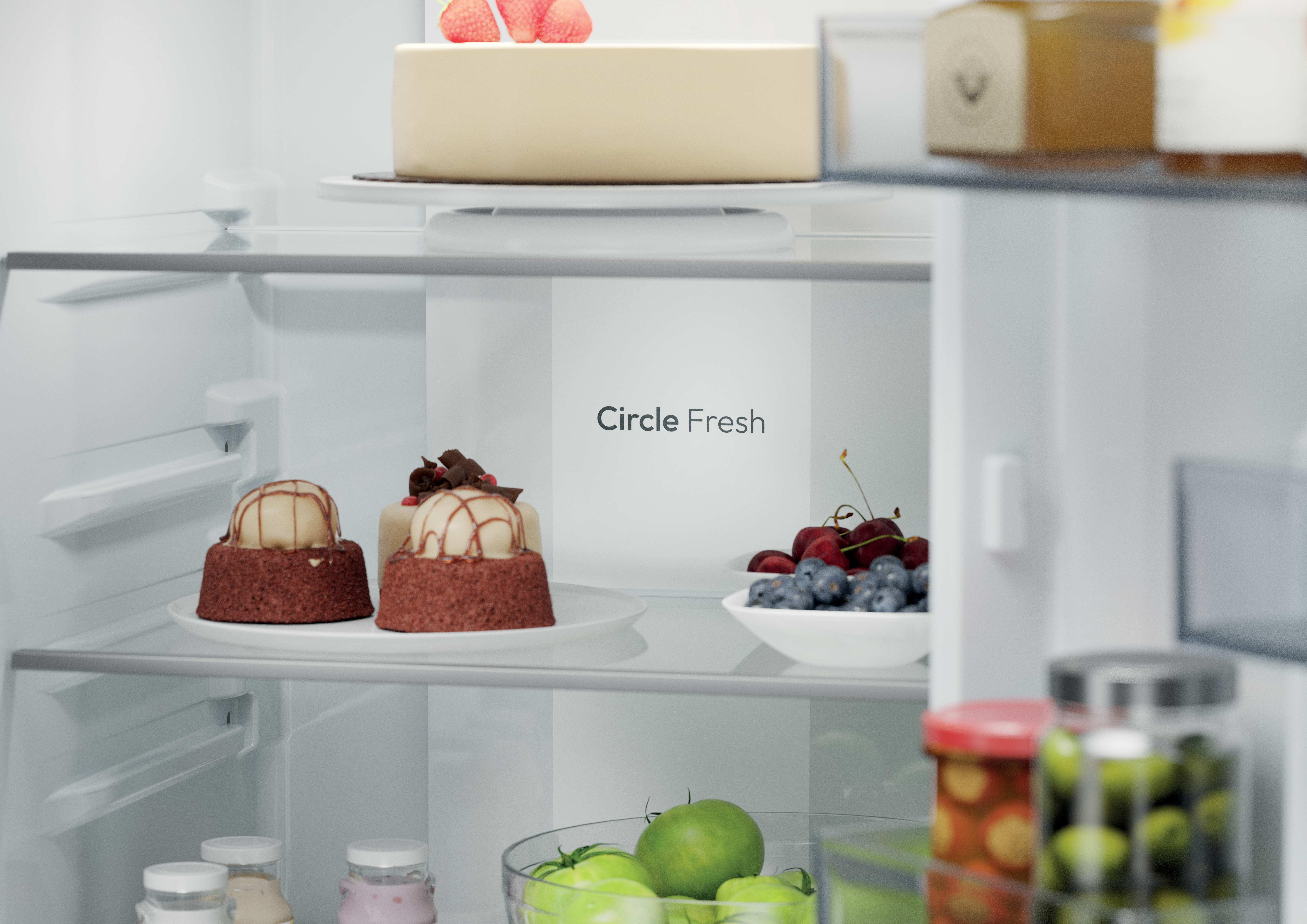 Interno di un frigorifero con torte, dessert e frutta sugli scaffali.
