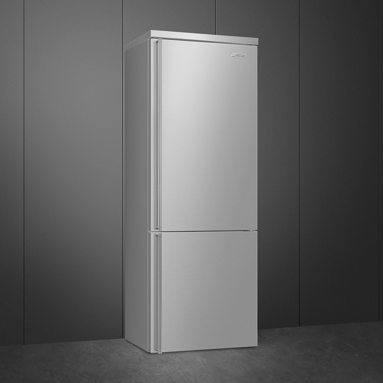 Un refrigerador Smeg plateado está contra una pared gris. Tiene una puerta superior e inferior.