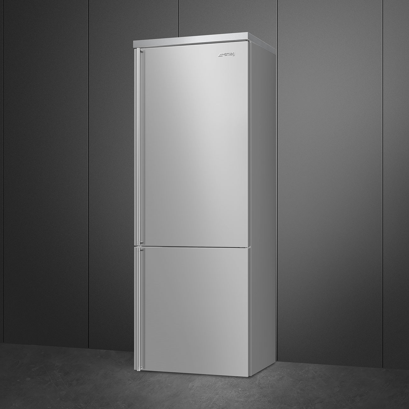 Un refrigerador plateado de dos puertas se encuentra frente a una pared y un piso gris oscuro.