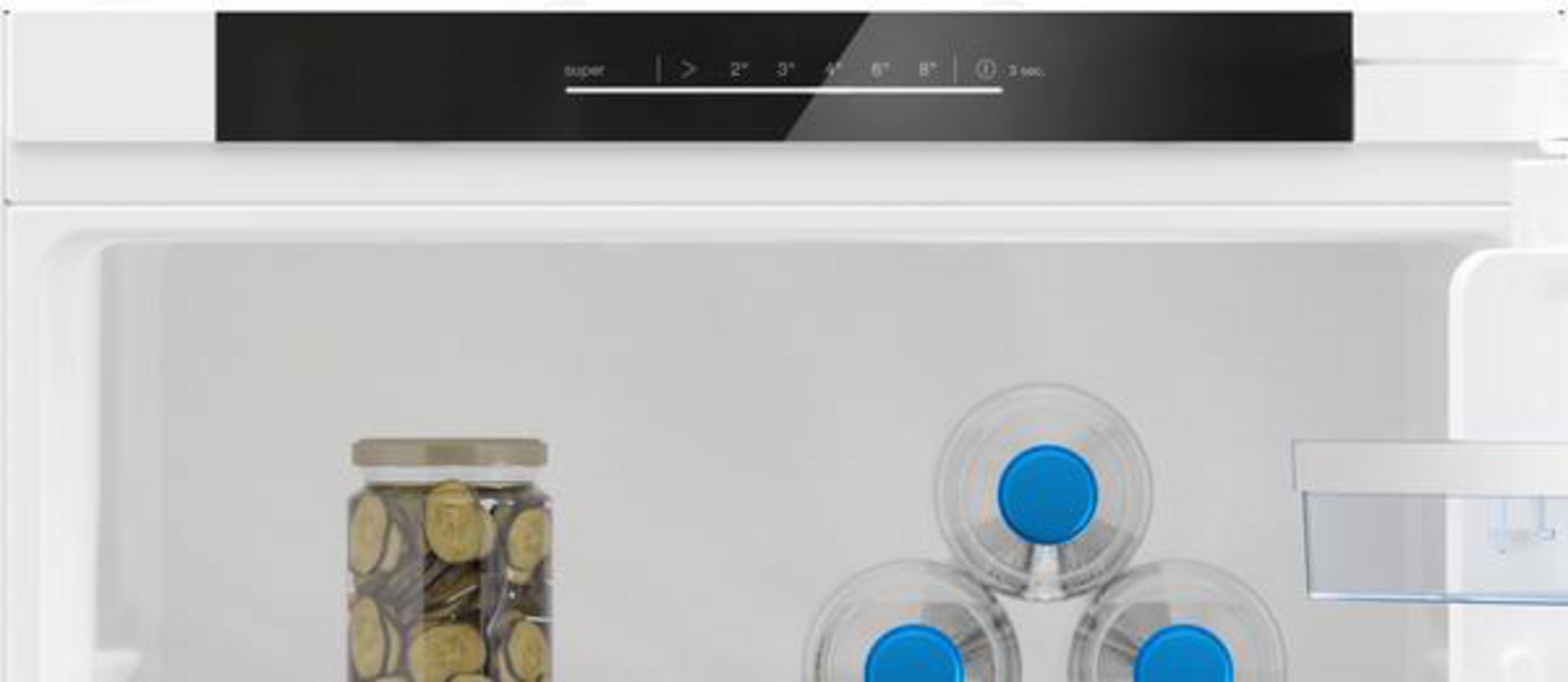 In einem weißen Kühlschrank mit Glaswasserflaschen und einem Glas voller Münzen. Digitalanzeige oben.