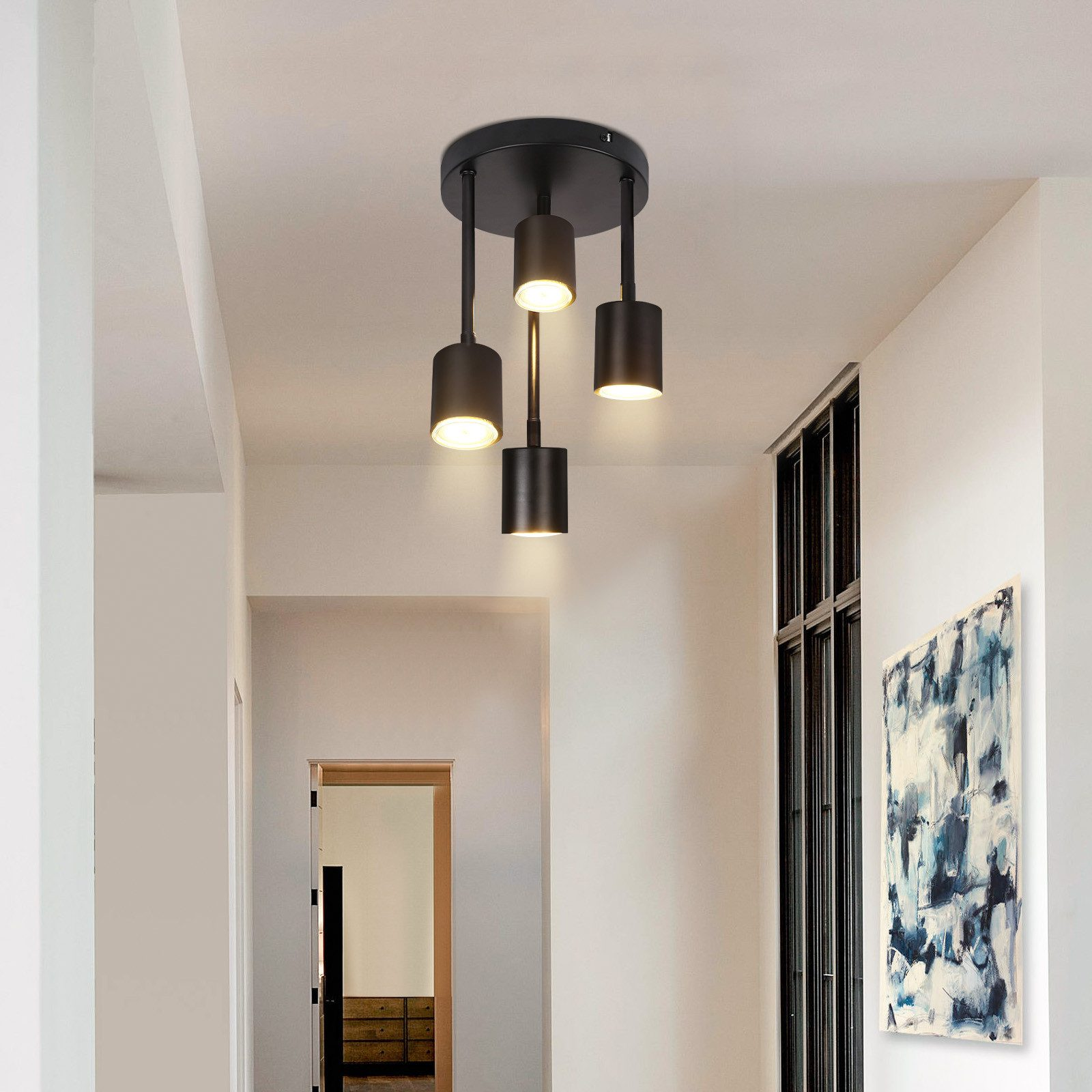 Czarna lampa sufitowa z trzema cylindrycznymi światłami. Korytarz z drzwiami i obrazem w tle.