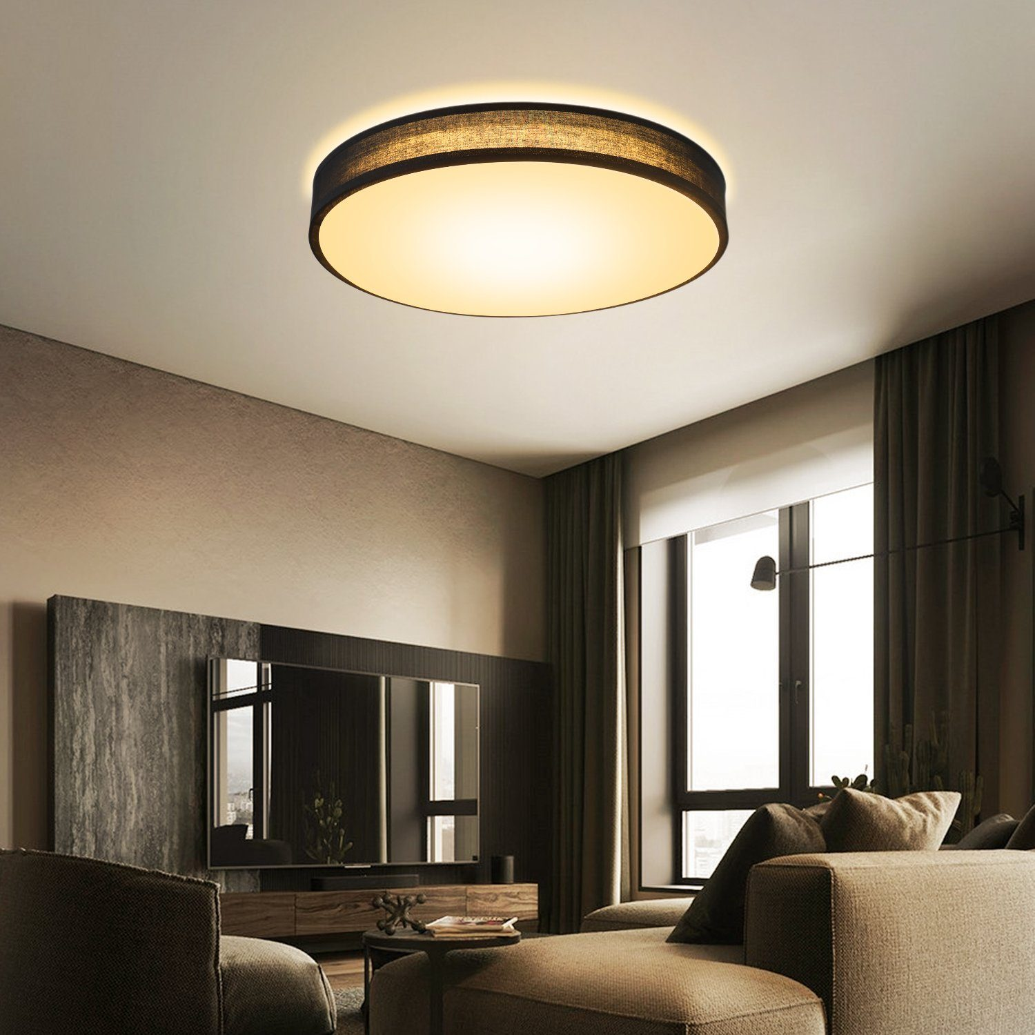 Runde, schwarze Deckenlampe, die ein Wohnzimmer ausleuchtet. Das Zimmer hat Sofa, TV und Vorhänge.