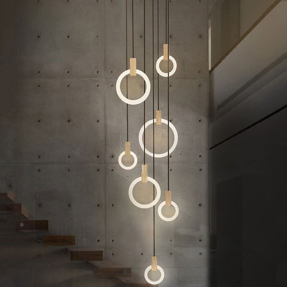 Moderne Hängeleuchte mit sieben beleuchteten Ringen, Holzakzenten und Betonwand im Hintergrund.
