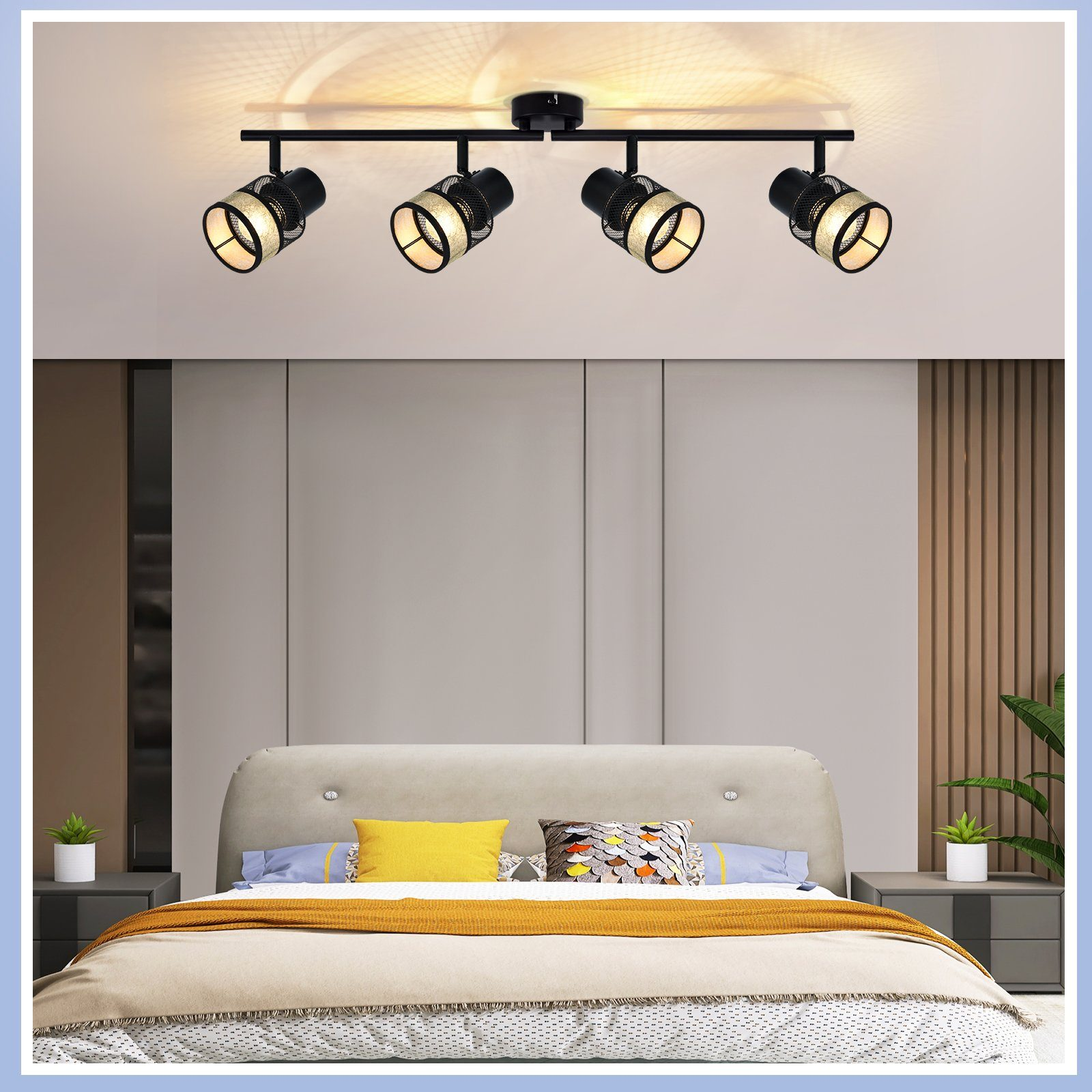 Camera da letto con illuminazione a binario. Quattro faretti neri sul soffitto. Letto con cuscini e piante.