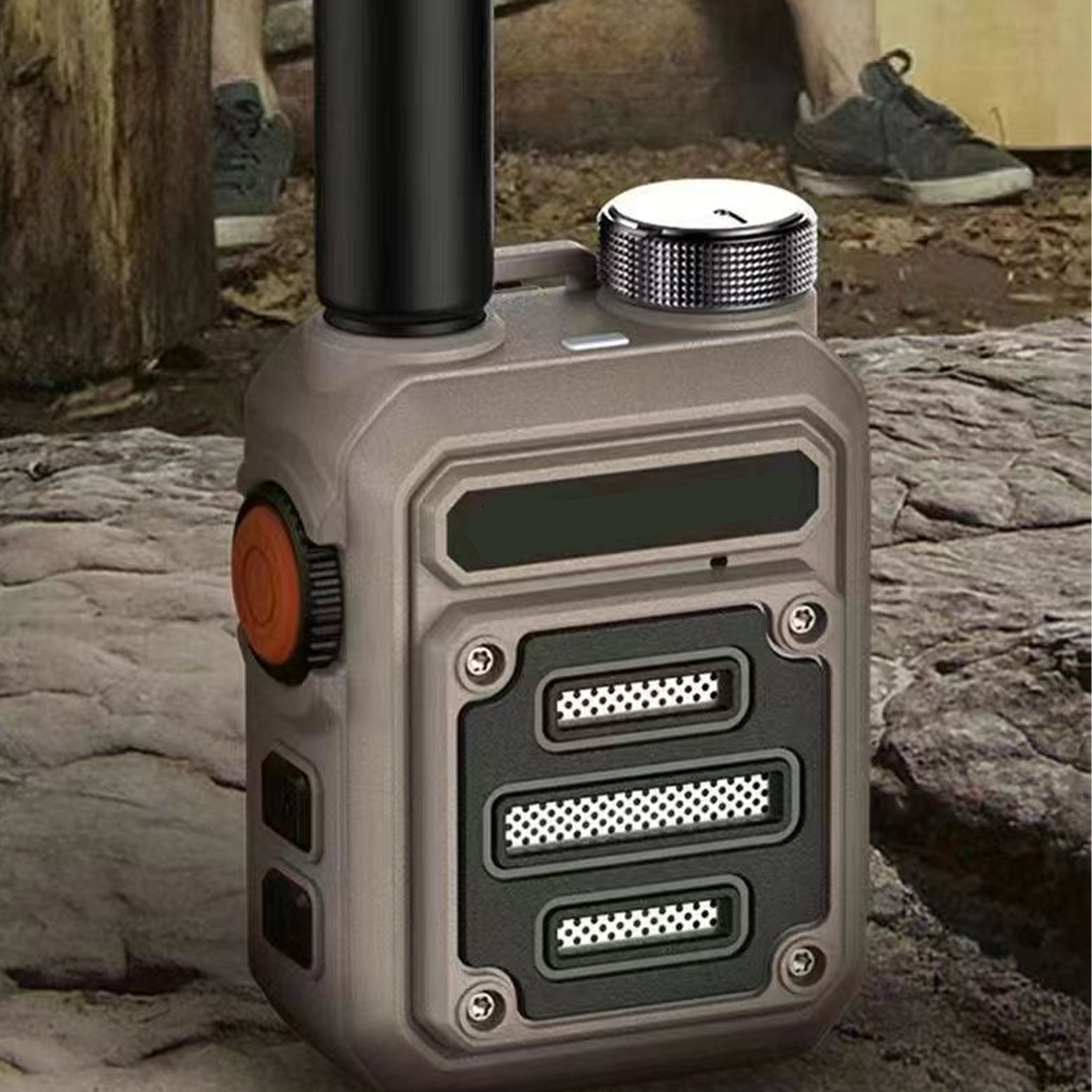 Ein graues und schwarzes Walkie-Talkie. Es hat einen orangen Knopf und eine Antenne. Im Hintergrund sind eine Person und Bäume zu sehen.
