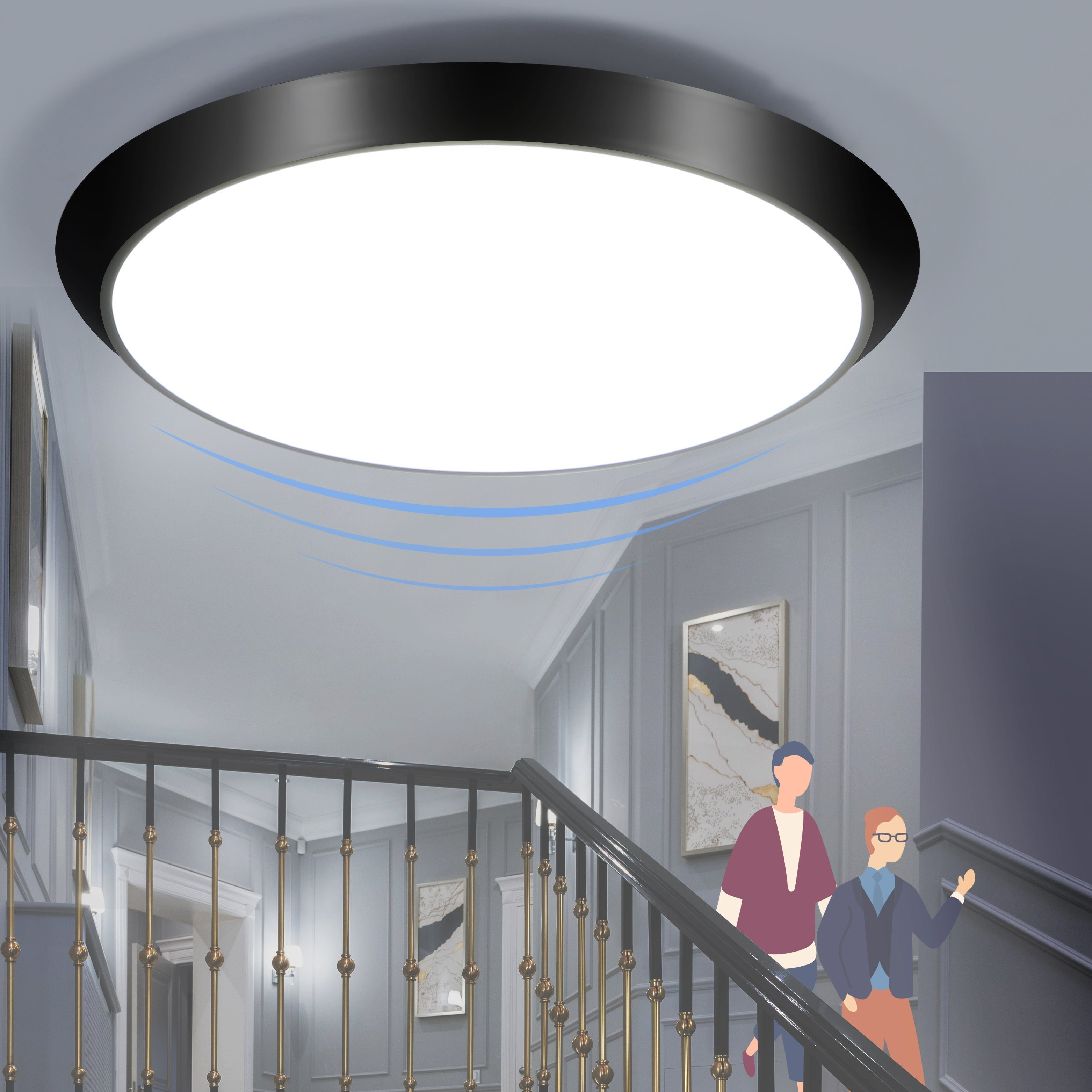 Jasna okrągła lampa sufitowa w korytarzu z ludźmi schodzącymi po schodach. Szare ściany i czarna balustrada.