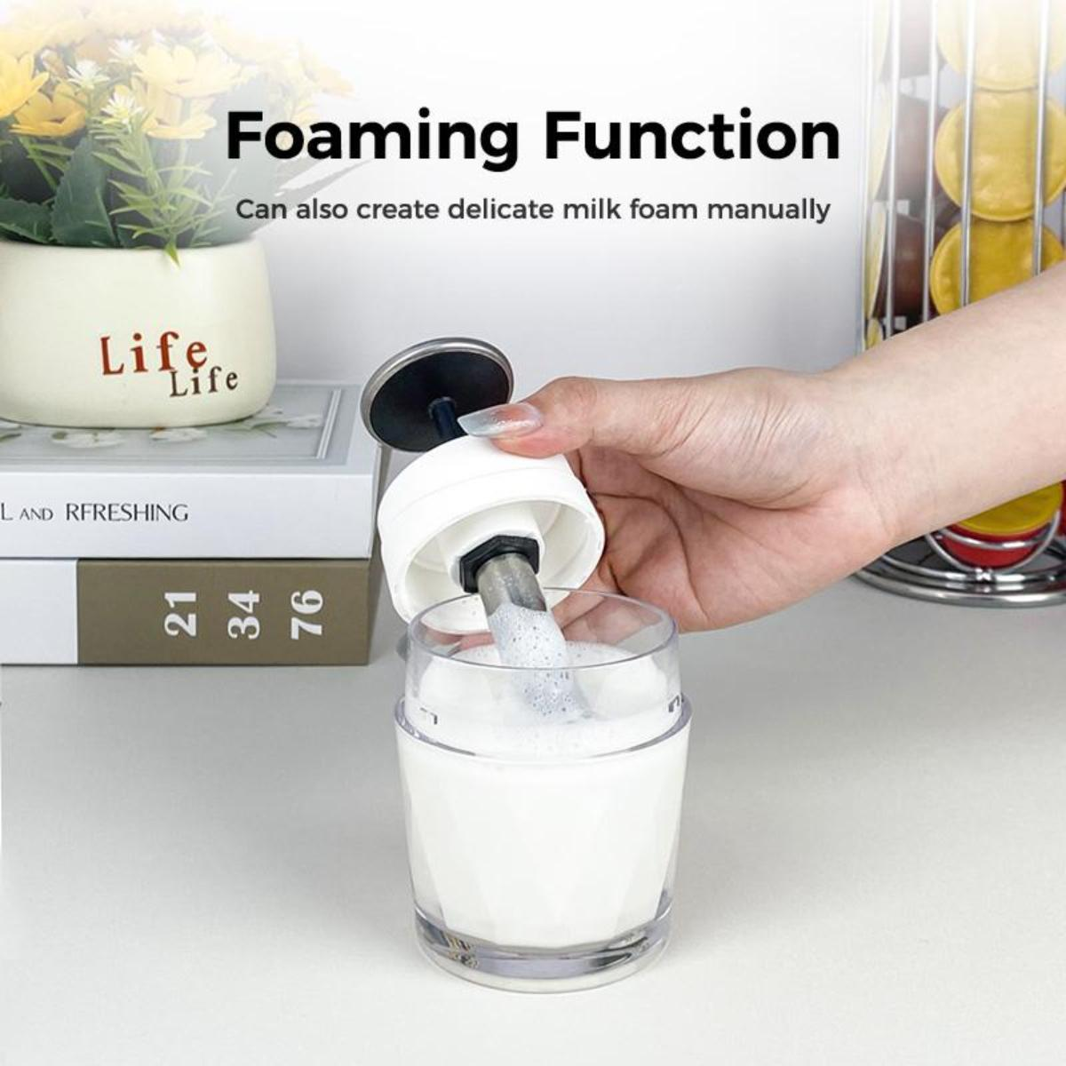 Eine Hand, die Milch aus einem Milchaufschäumer in ein Glas gießt. Bücher und ein dekorativer Gegenstand im Hintergrund.