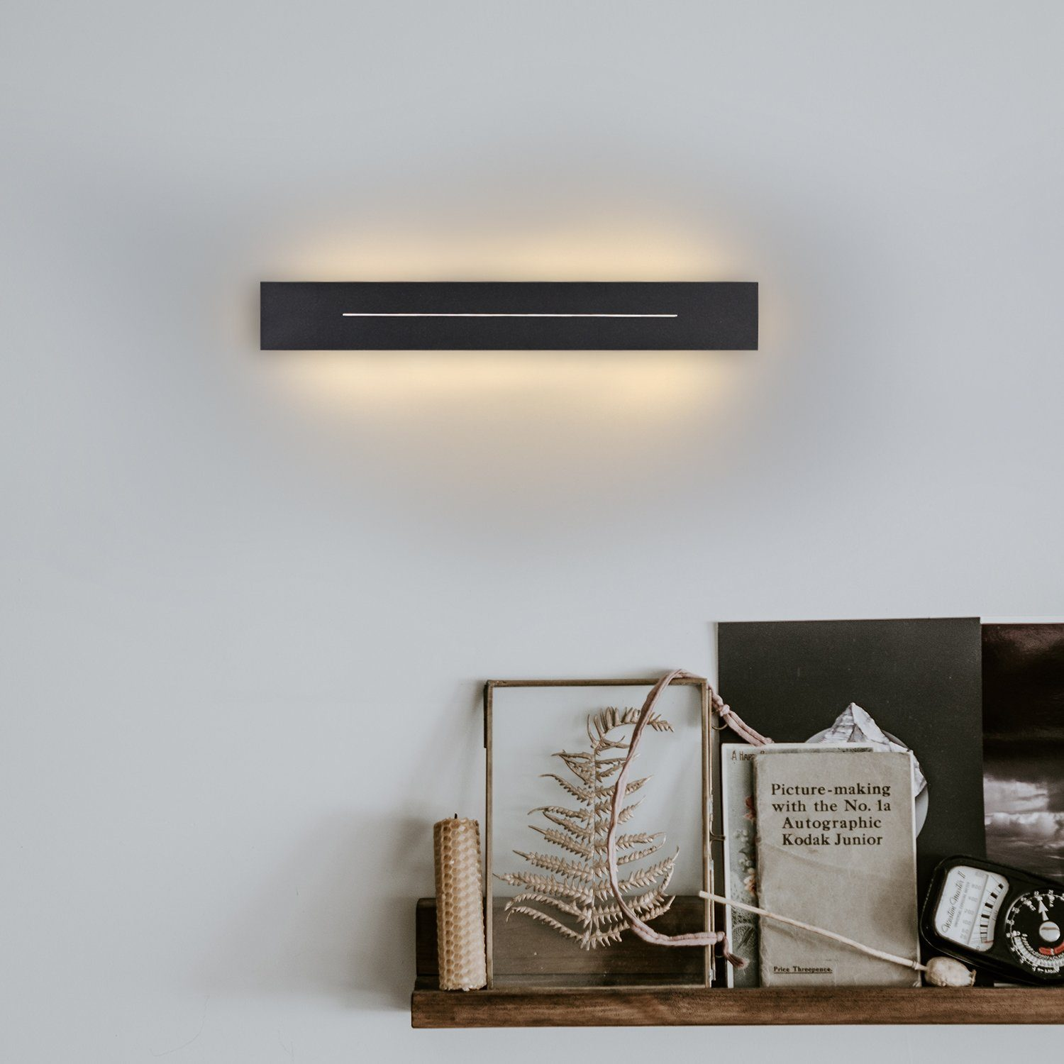 Applique nera. Libri e una candela su una mensola di legno sotto la lampada.