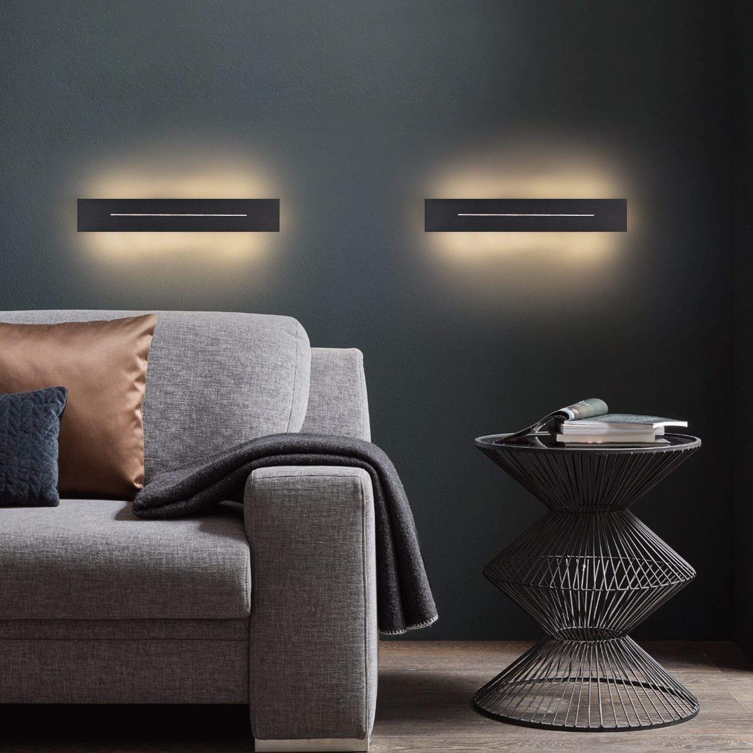 Interni. Divano grigio. Due applique nere che emettono luce calda. Tavolo rotondo.
