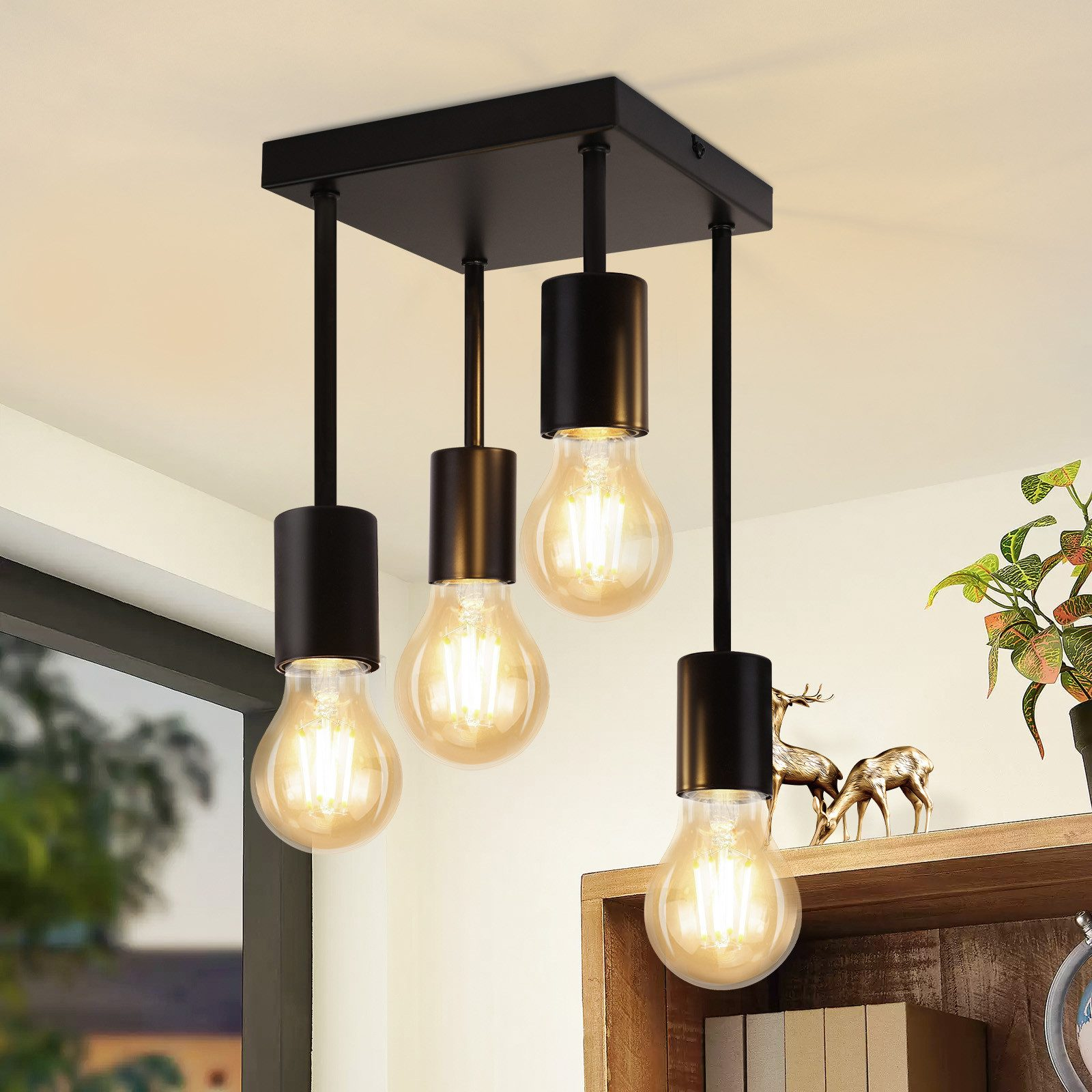 Eine Gruppe von vier Glühbirnen, die an einer schwarzen Deckenleuchte hängen. Die Glühbirnen sind im Edison-Stil.
