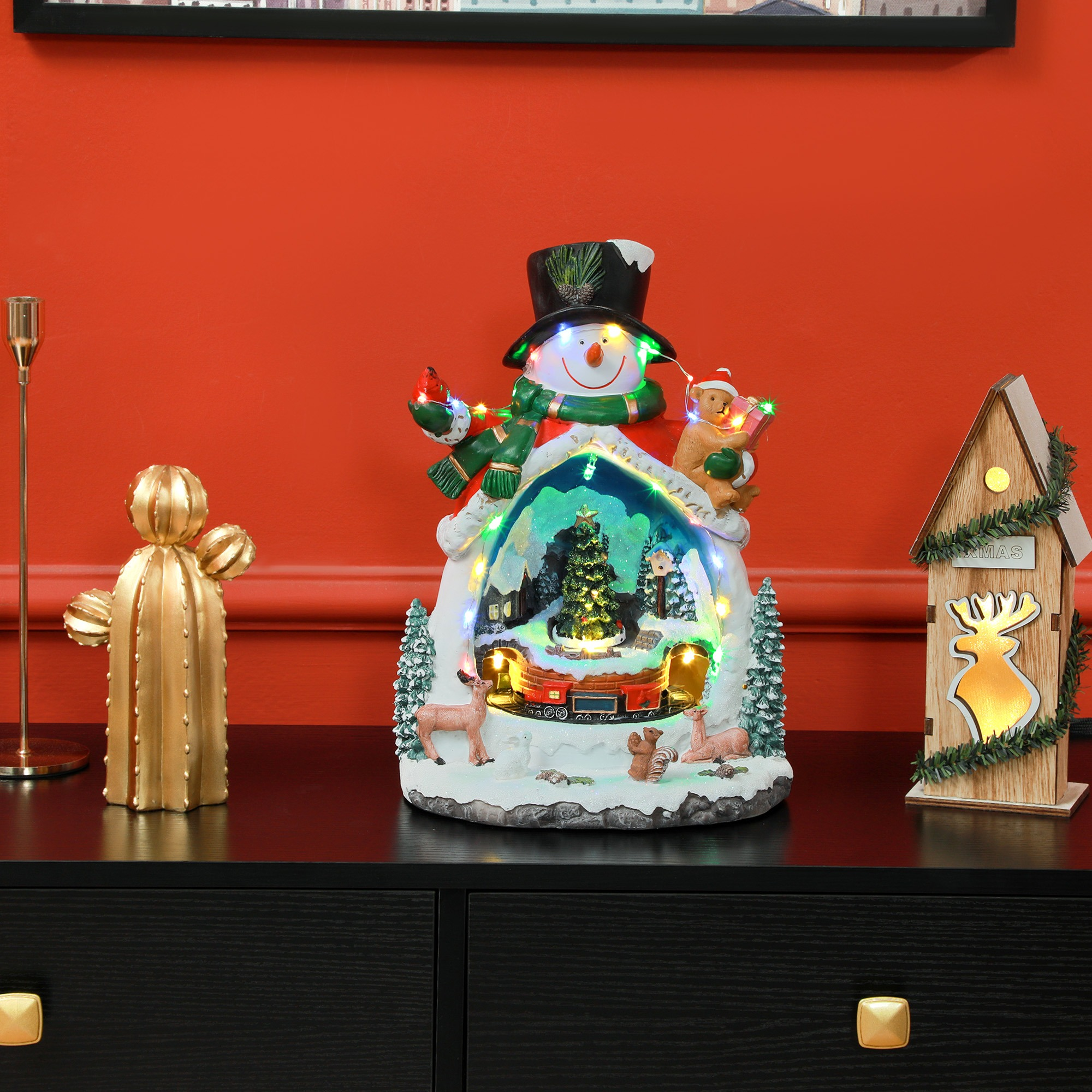 Schneemann-Weihnachtsschmuck auf einem Tisch mit anderen Dekorationen und roter Wand.