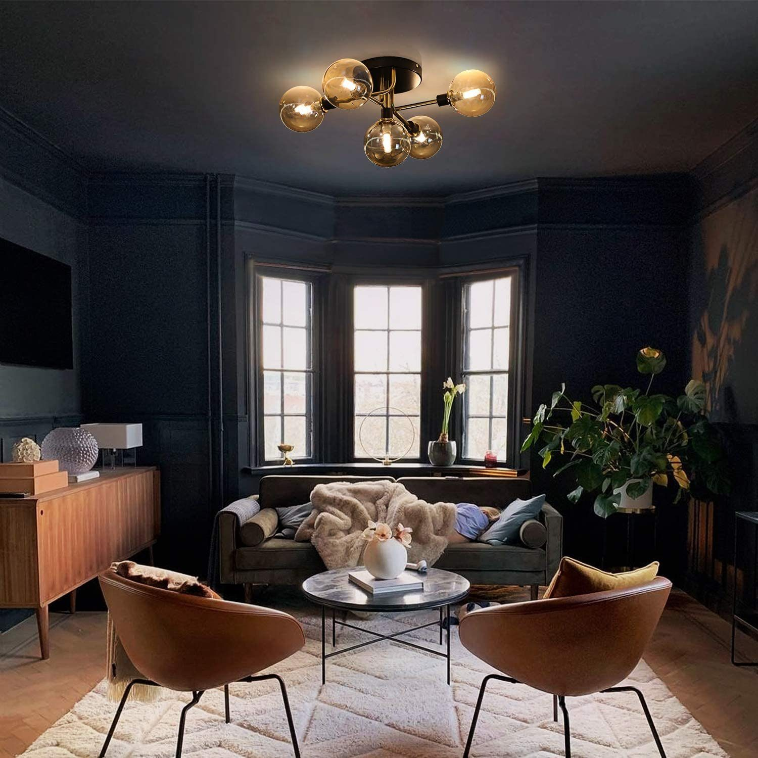 Ein Raum mit schwarzer Decke und Deckenleuchte. Es gibt eine Couch, Stühle und einen Tisch. Ein Fenster ist im Hintergrund.