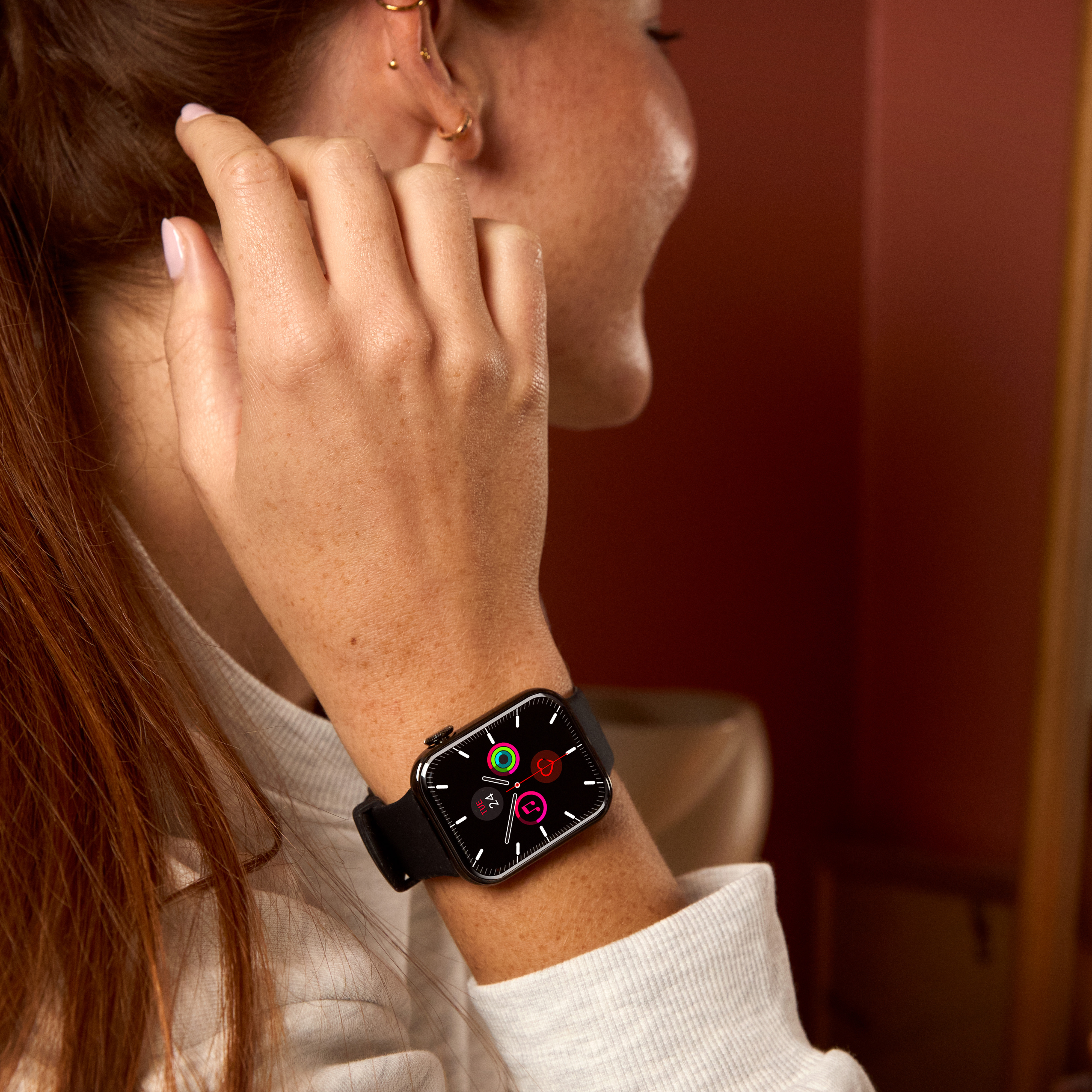 Bras de femme avec une smartwatch noire. Écran affiche des icônes colorées. Elle porte un haut blanc.