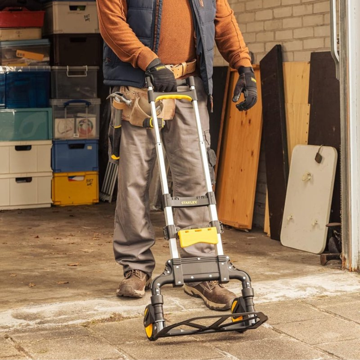 A person in work clothes holding a Stanley hand truck in a storage area.