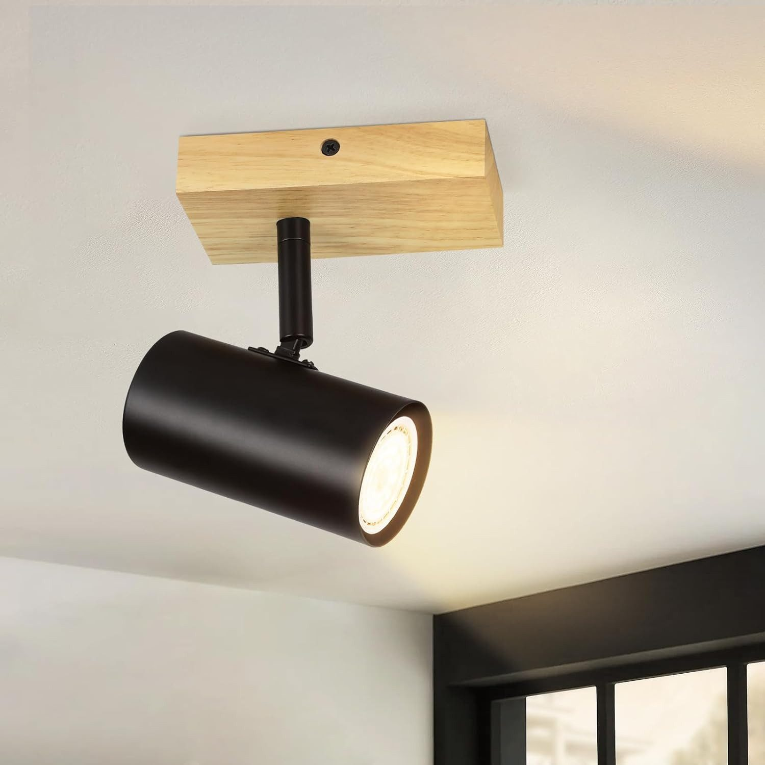 Un faretto nero è montato su una base di legno sul soffitto, con la luce che brilla verso il basso.