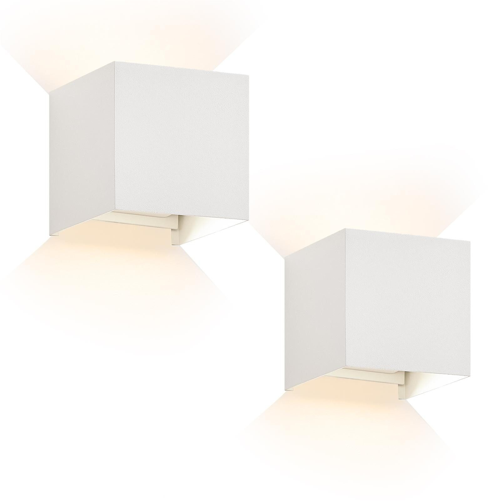 Due luci da parete bianche a forma di cubo, ognuna emette luce verso il basso e verso l'esterno.