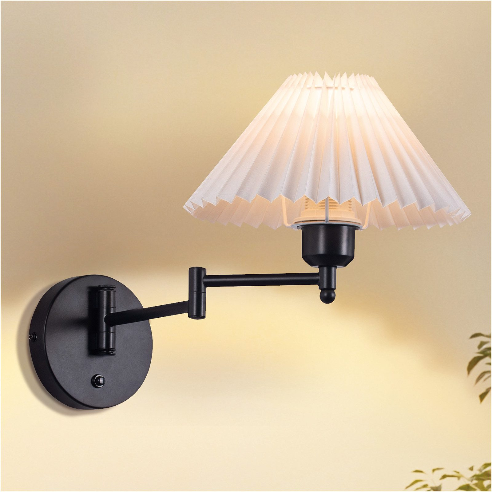 Lampada da parete nera con paralume bianco plissettato, montata su parete gialla.