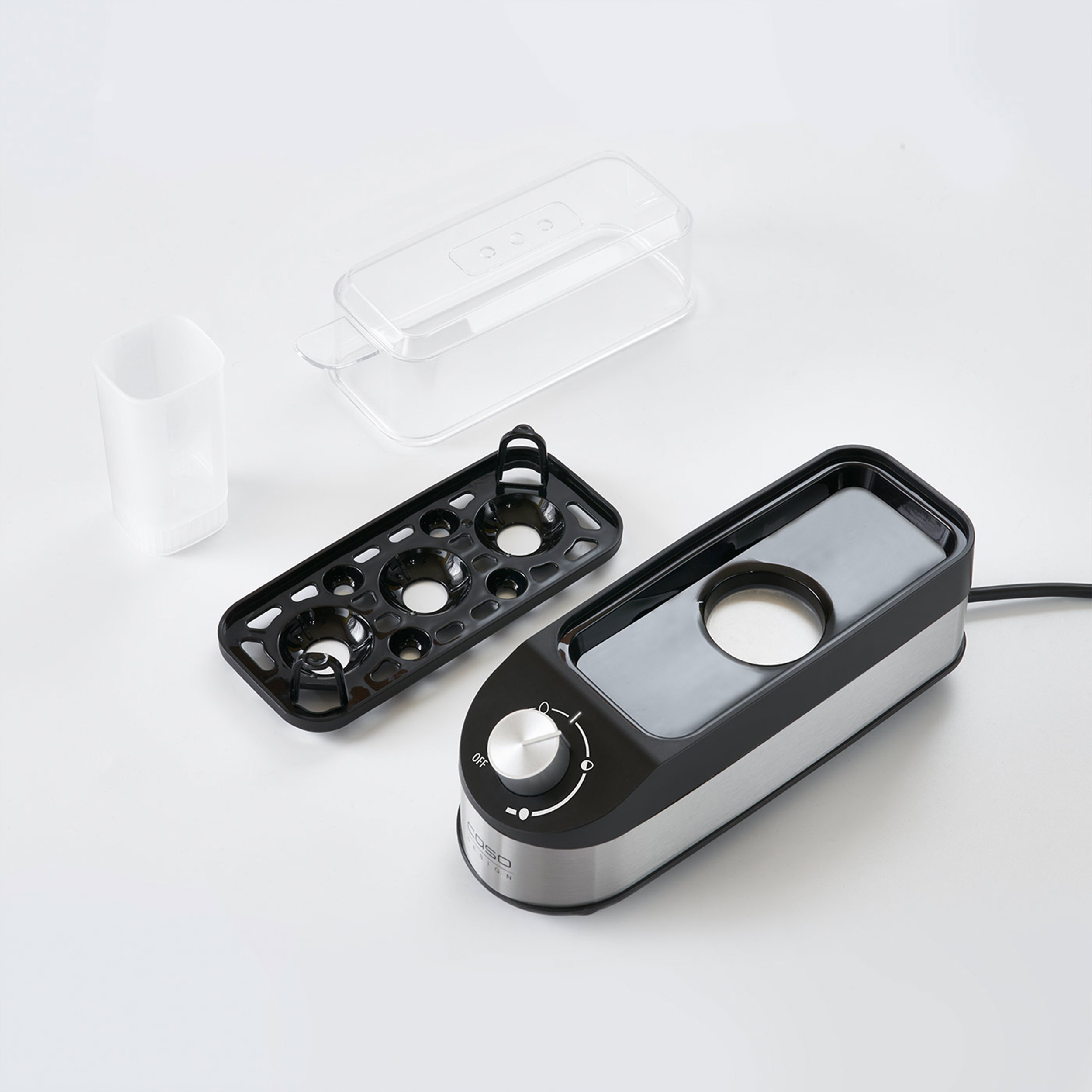 Elementy urządzenia do gotowania jajek: czarna podstawa, przezroczysta pokrywa i czarna taca z otworami.